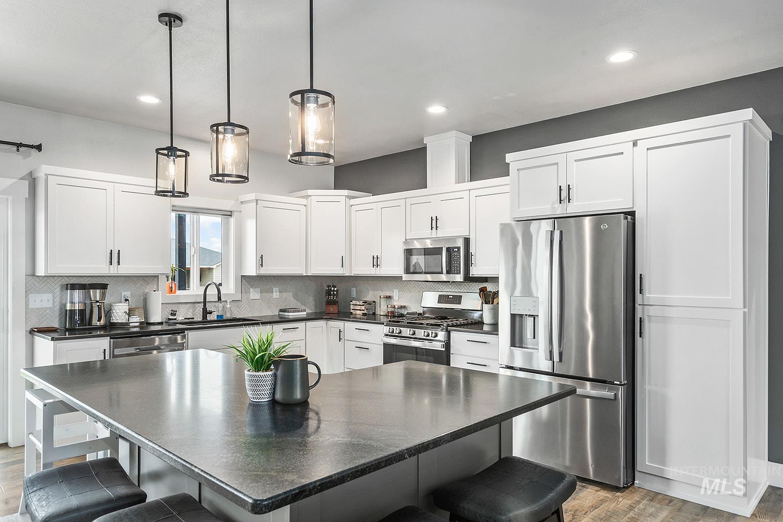 Kitchen with a breakfast bar area, stainless steel appliances, decorative light fixtures, white cabinets, and recessed lighting