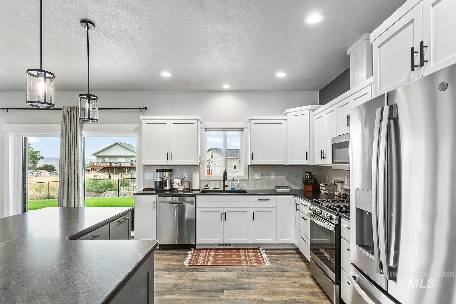 Kitchen with dark countertops, appliances with stainless steel finishes, pendant lighting, white cabinetry, and dark wood finished floors