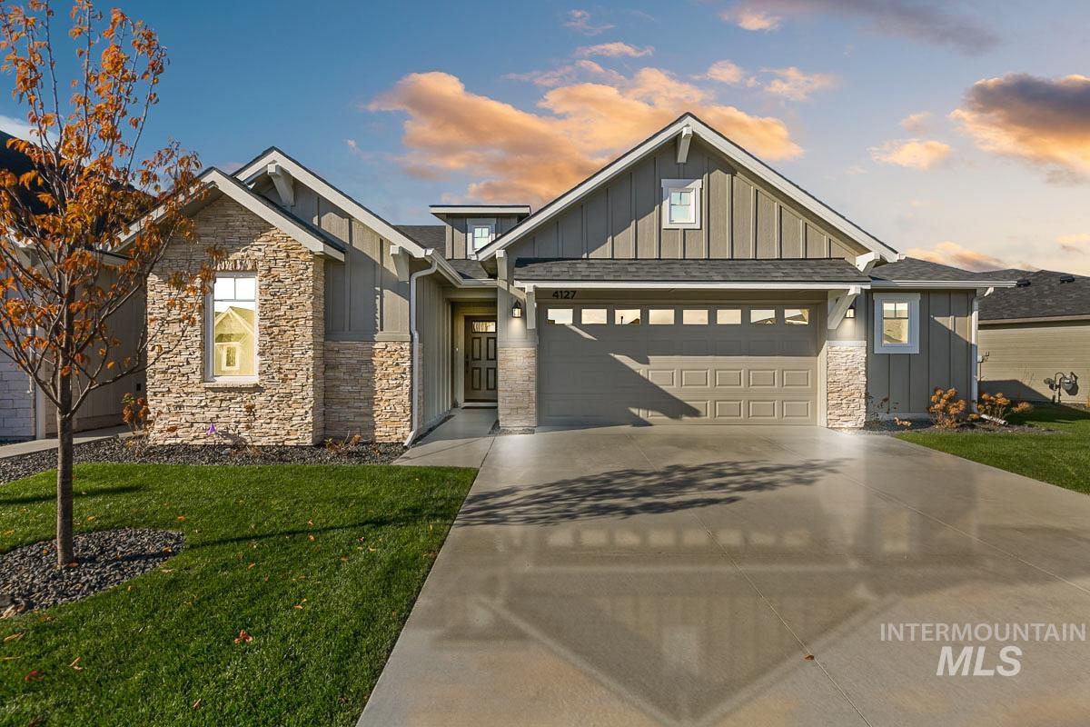 Craftsman-style home with board and batten siding, stone siding, a front lawn, and concrete driveway