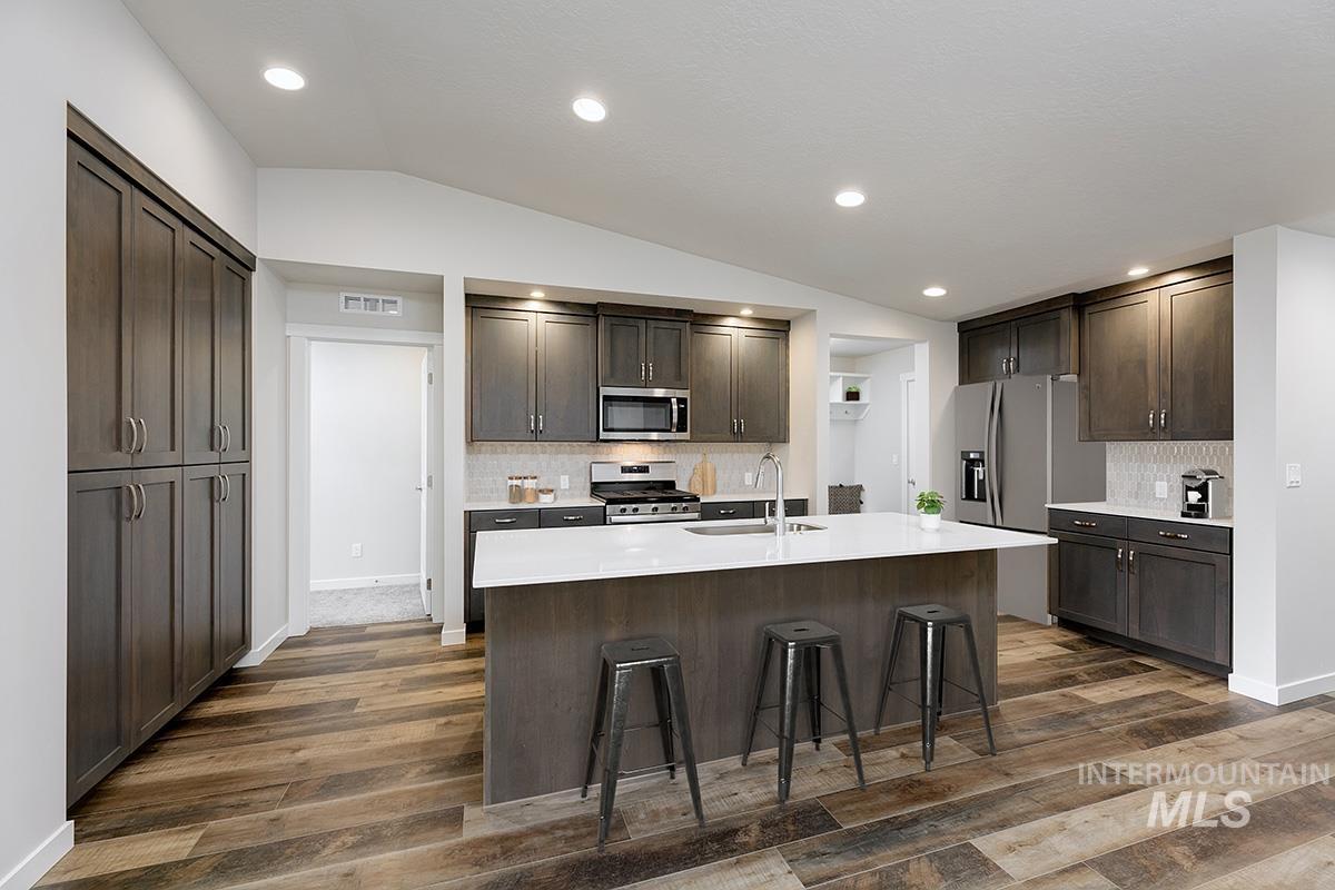 Kitchen with vaulted ceiling, decorative backsplash, stainless steel appliances, a breakfast bar, and recessed lighting