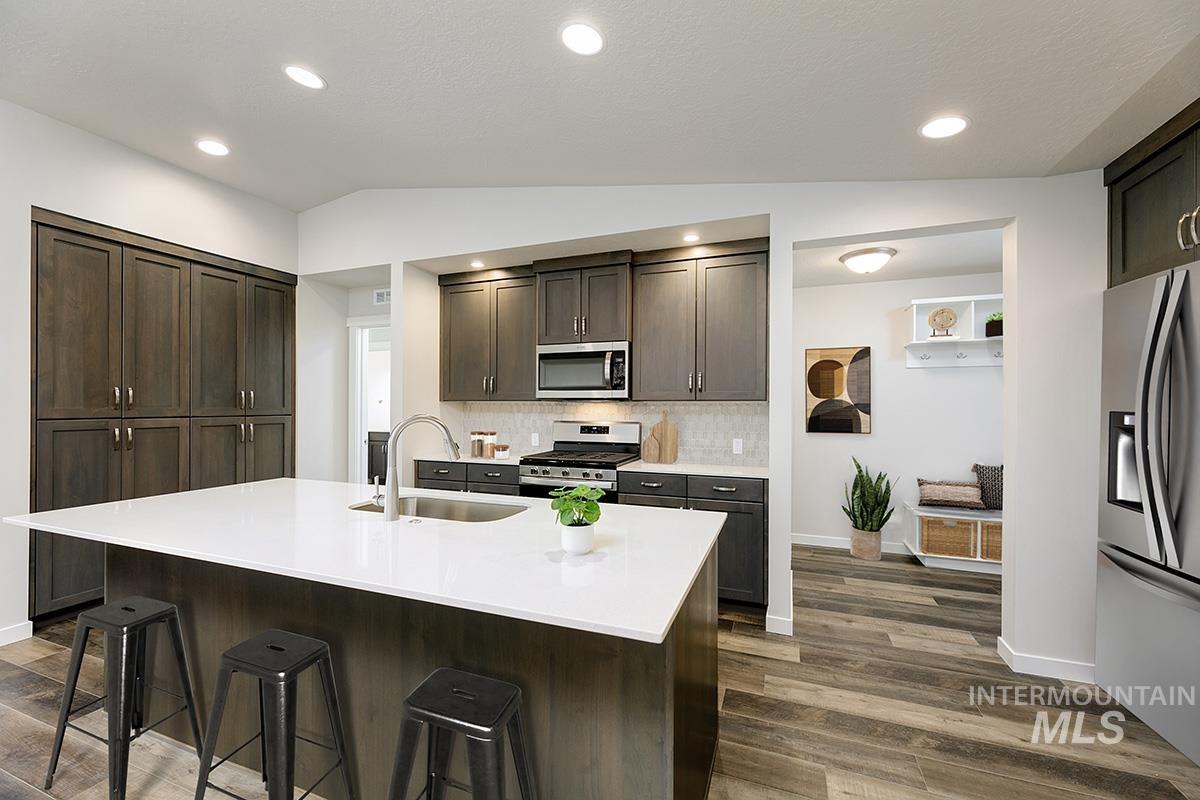 Kitchen featuring vaulted ceiling, appliances with stainless steel finishes, tasteful backsplash, dark brown cabinets, and dark wood-style flooring
