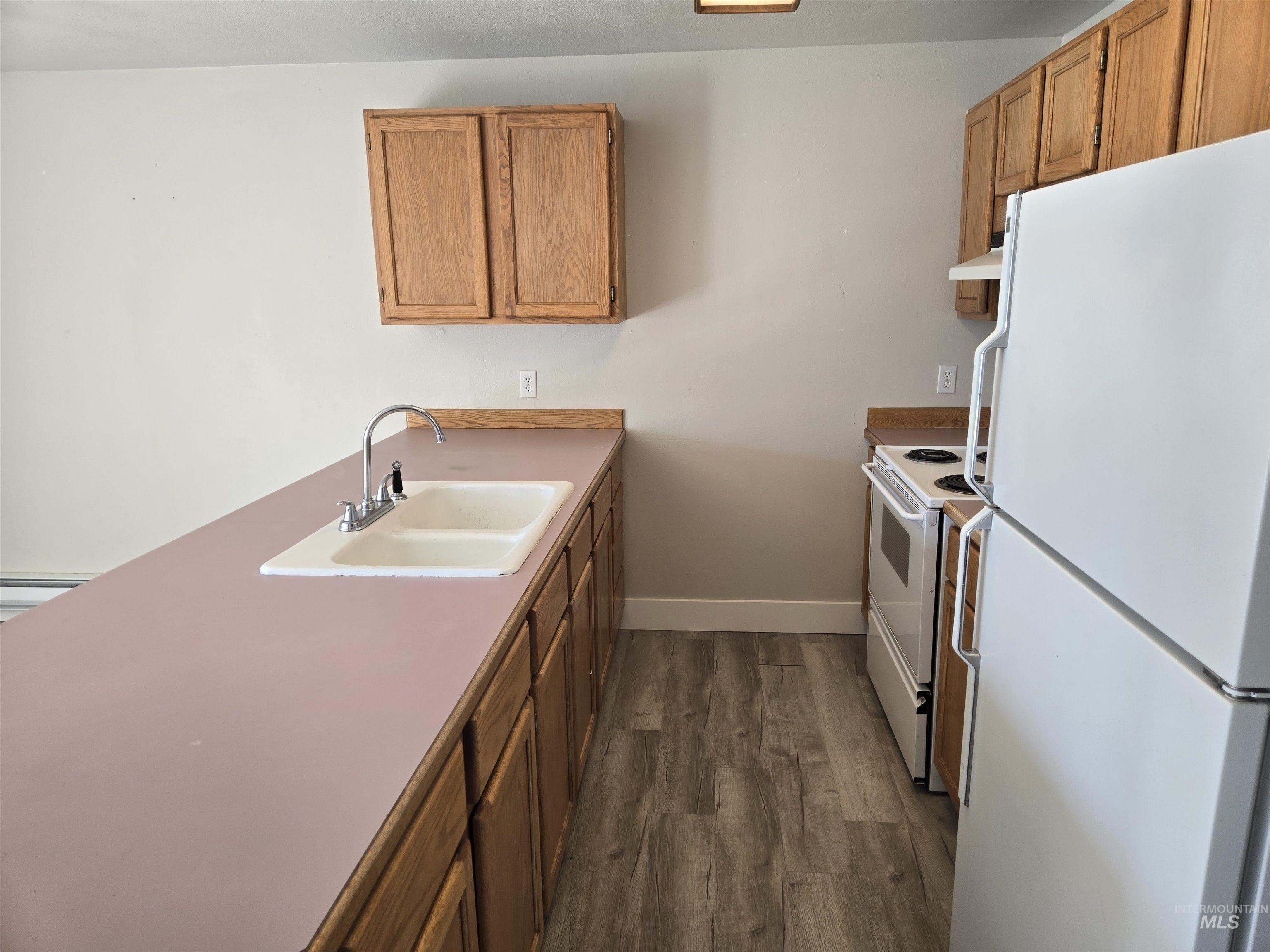 Kitchen with white appliances, dark wood finished floors, brown cabinets, and a peninsula