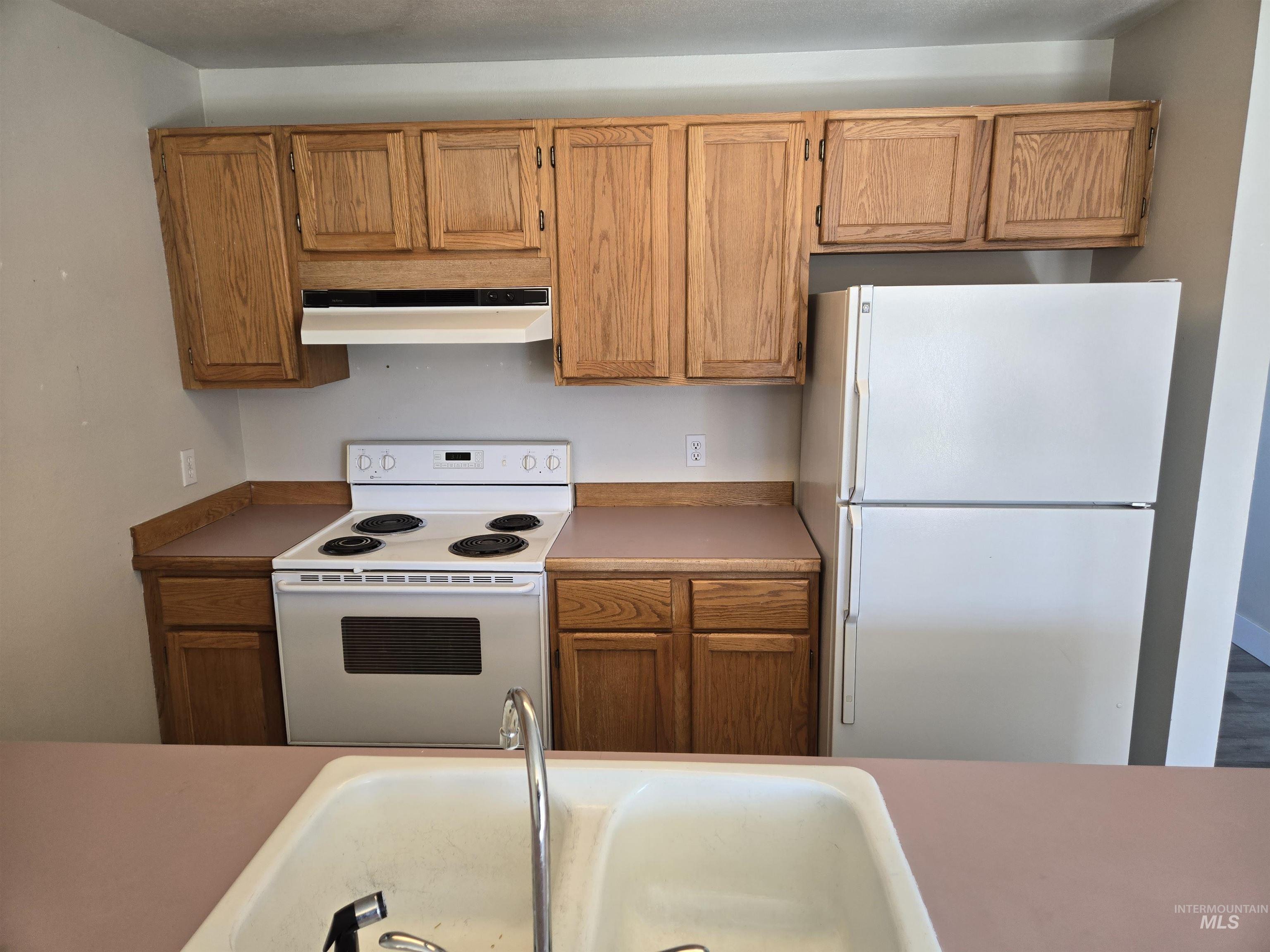 Kitchen with white appliances, under cabinet range hood, brown cabinets, and light countertops