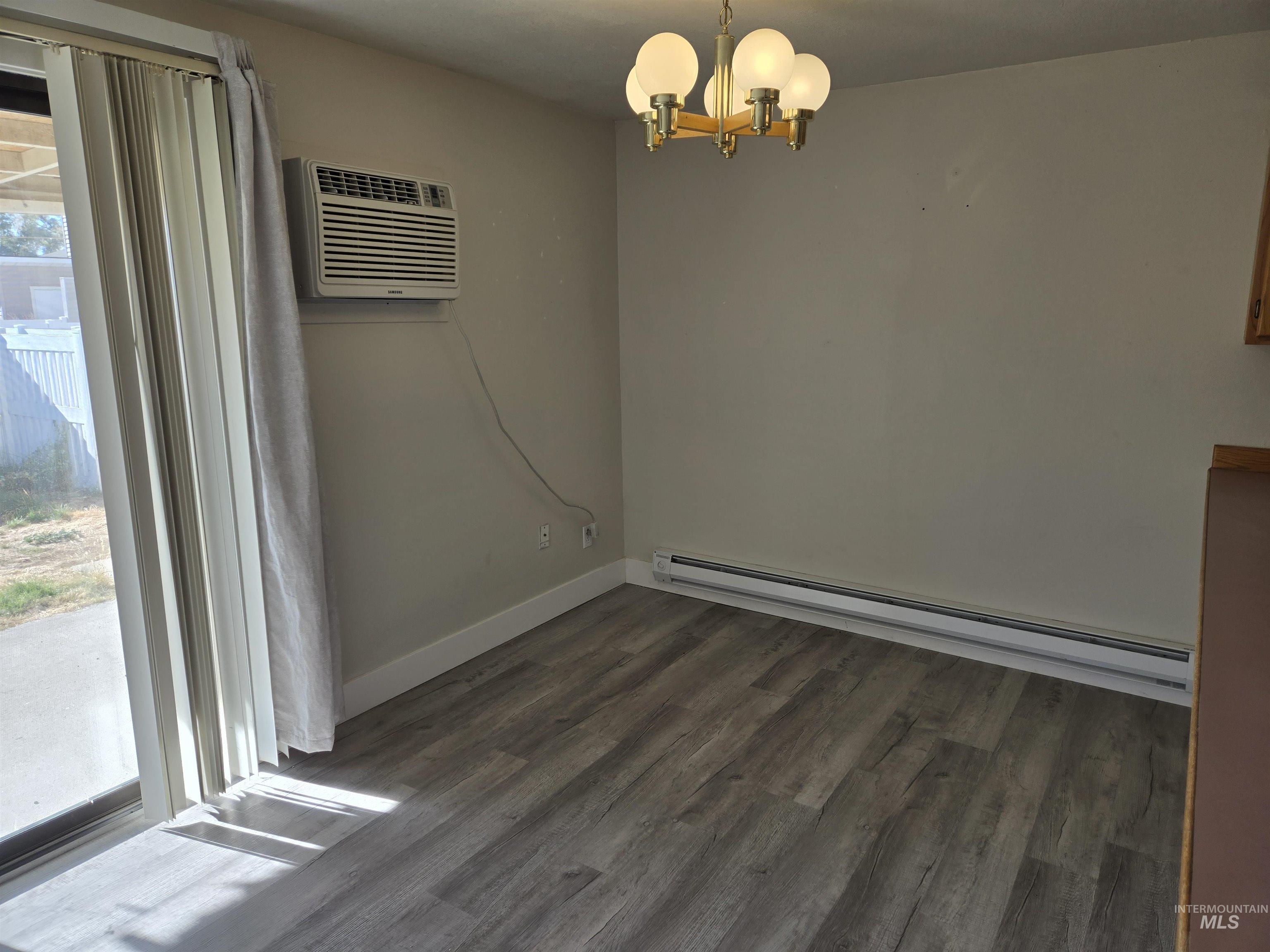 Unfurnished dining area with a baseboard radiator, dark wood finished floors, a chandelier, and a wall mounted AC