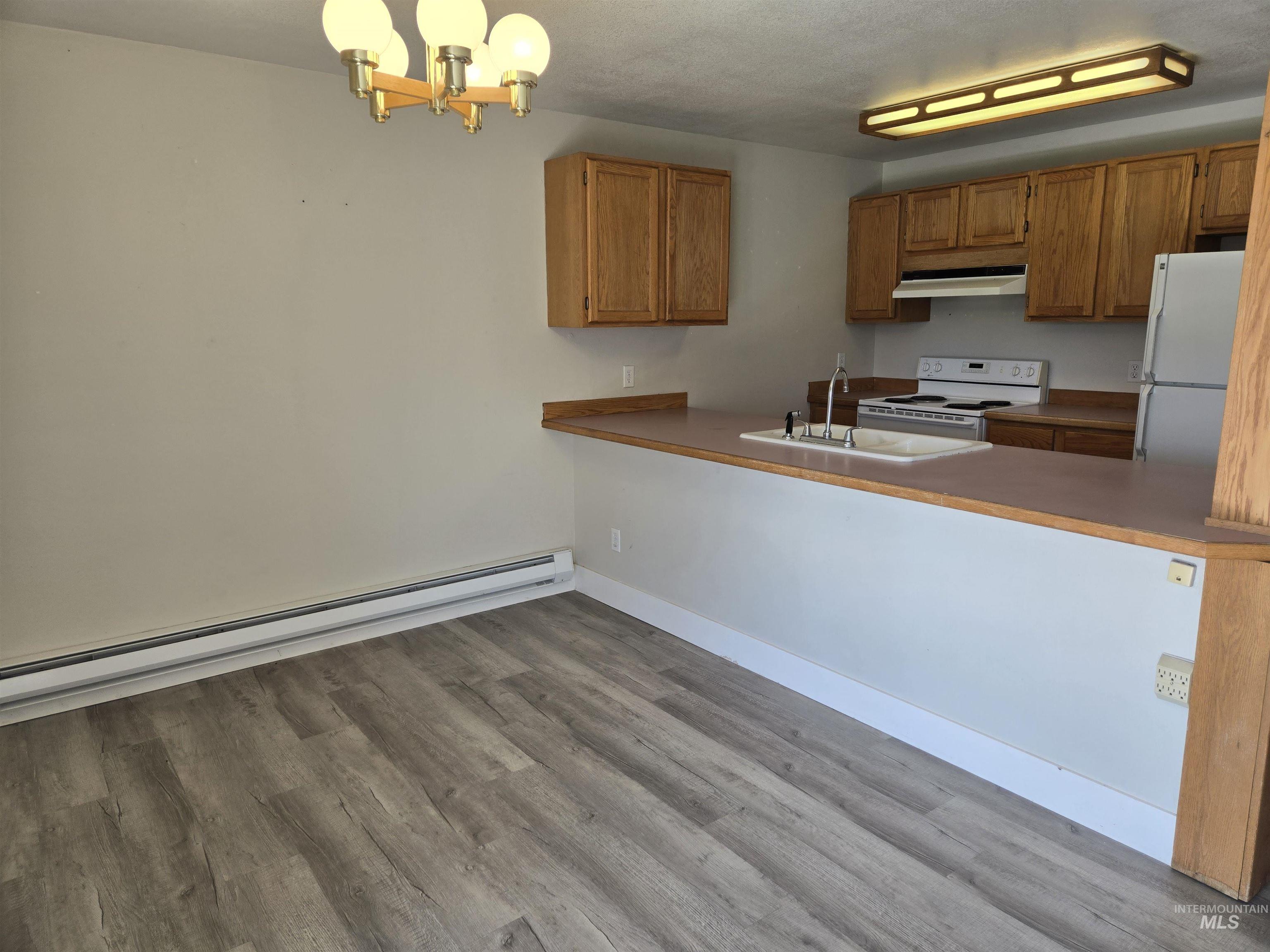Kitchen featuring a baseboard radiator, white appliances, pendant lighting, a chandelier, and light wood-style floors