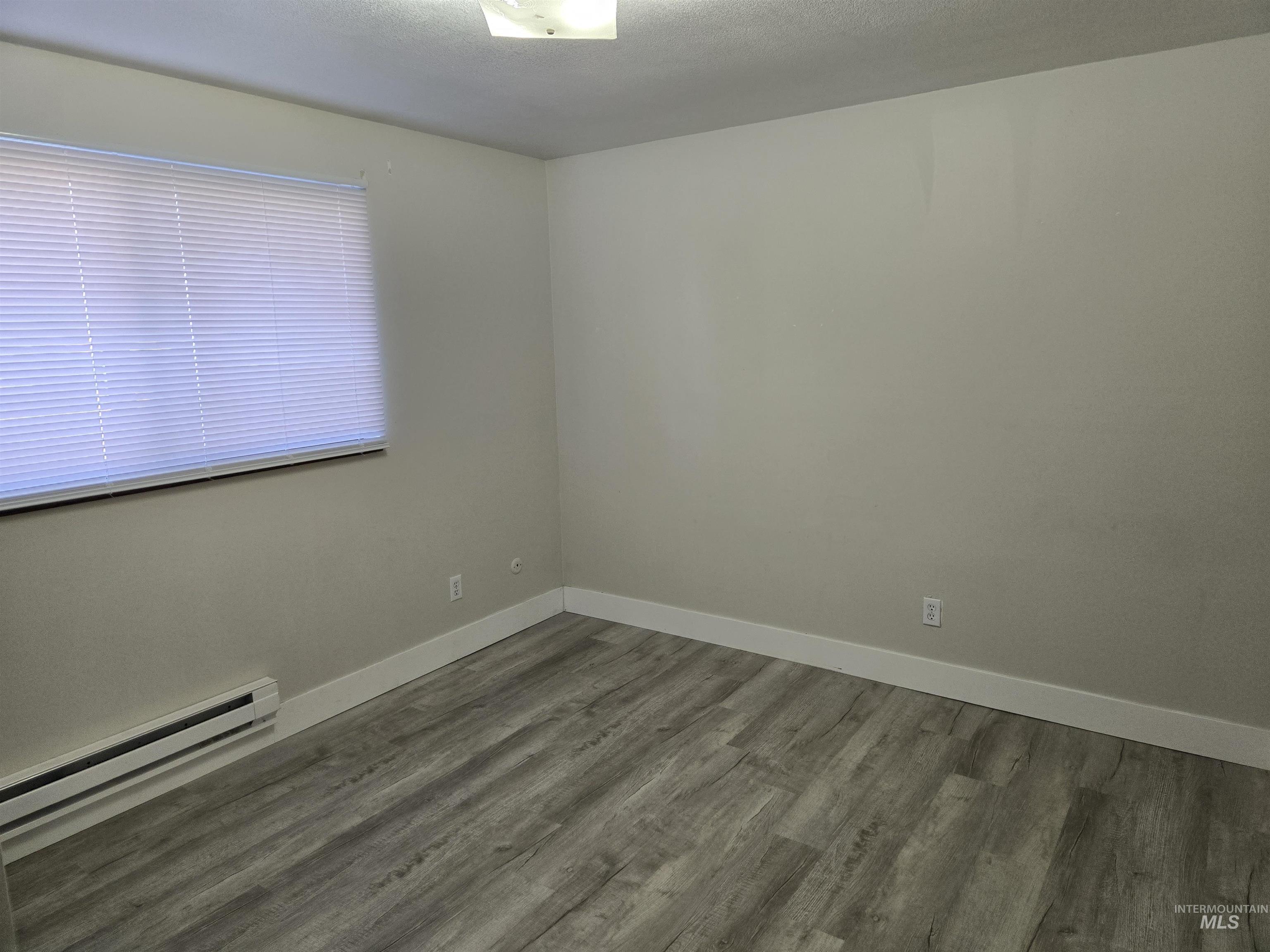 Spare room with a baseboard radiator, wood finished floors, and a textured ceiling