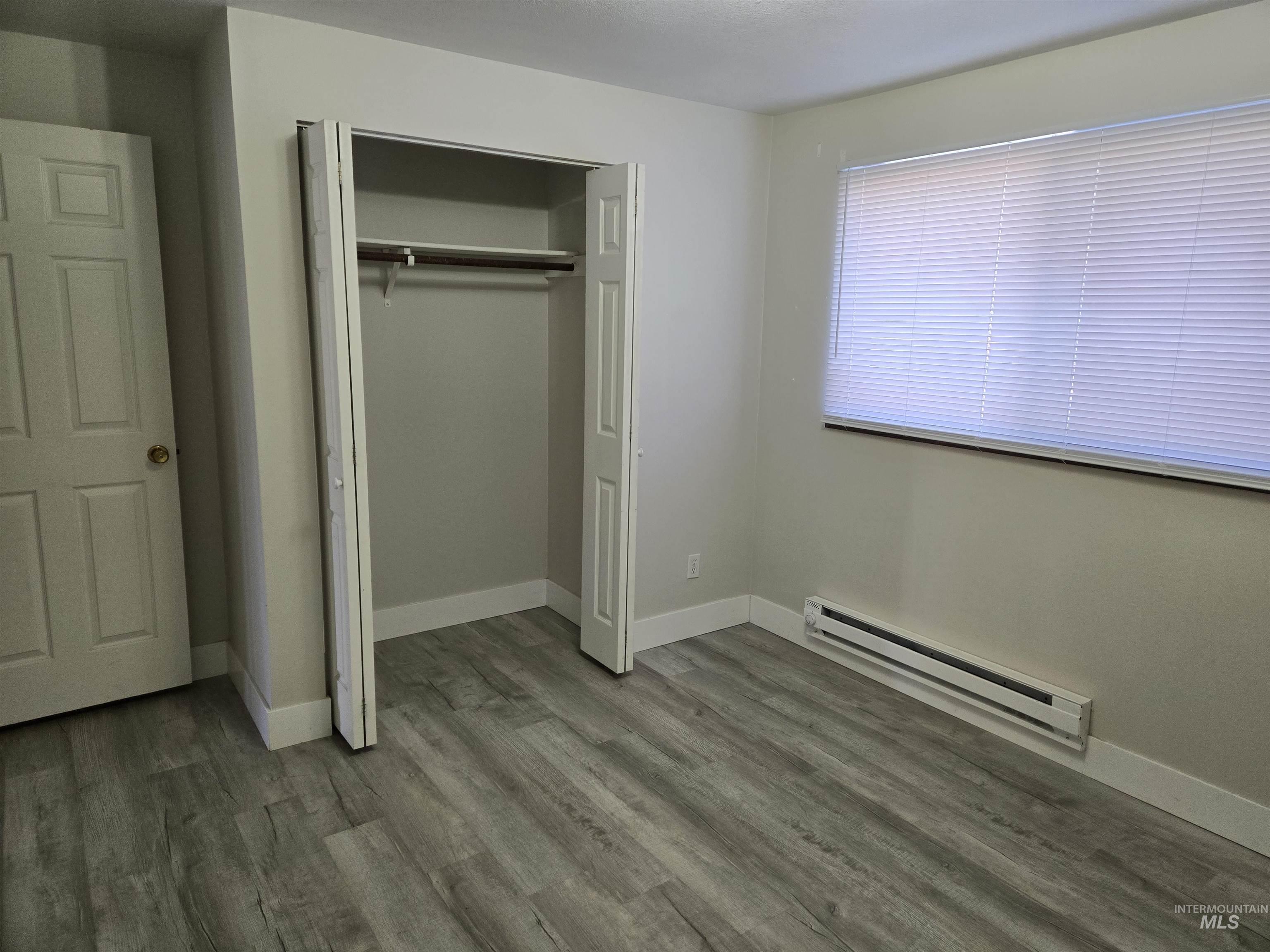 Unfurnished bedroom with a baseboard radiator, wood finished floors, and a closet