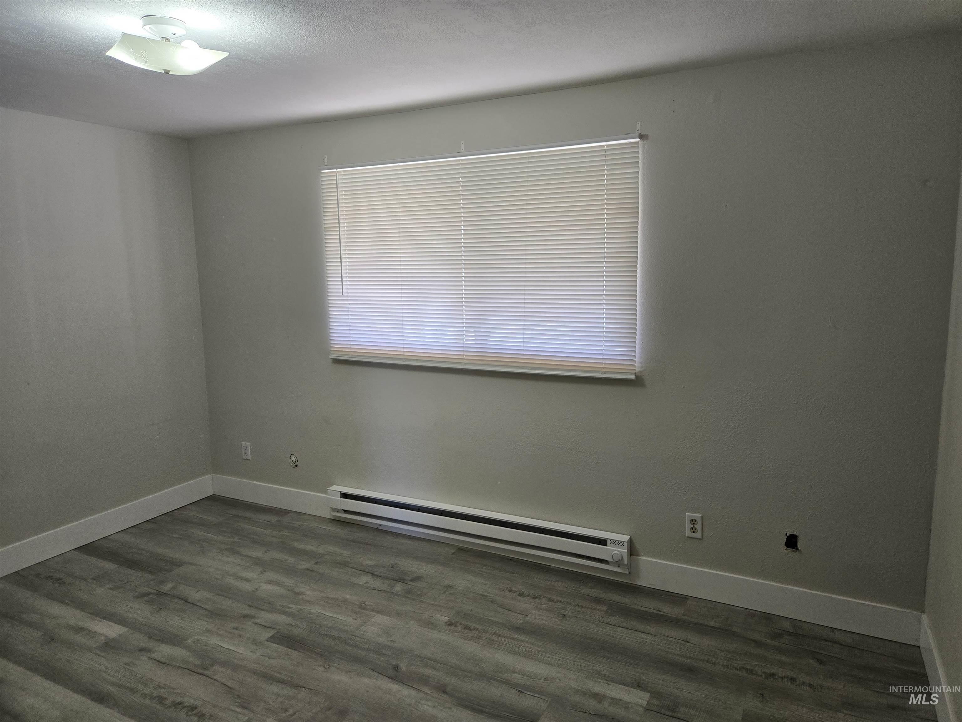 Spare room featuring a baseboard heating unit, dark wood-type flooring, and a textured ceiling