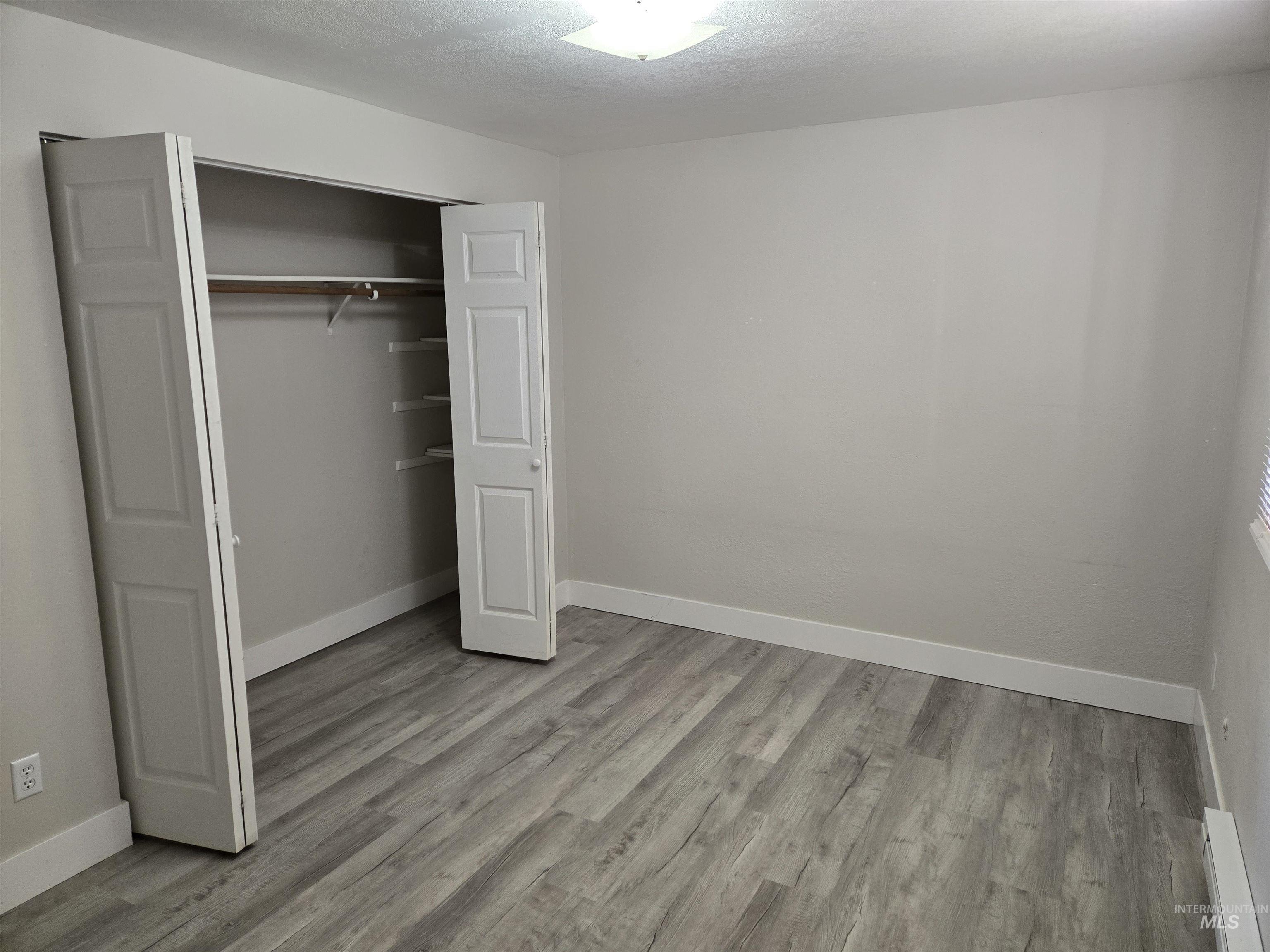 Unfurnished bedroom with a textured ceiling, light wood finished floors, a closet, and a baseboard heating unit