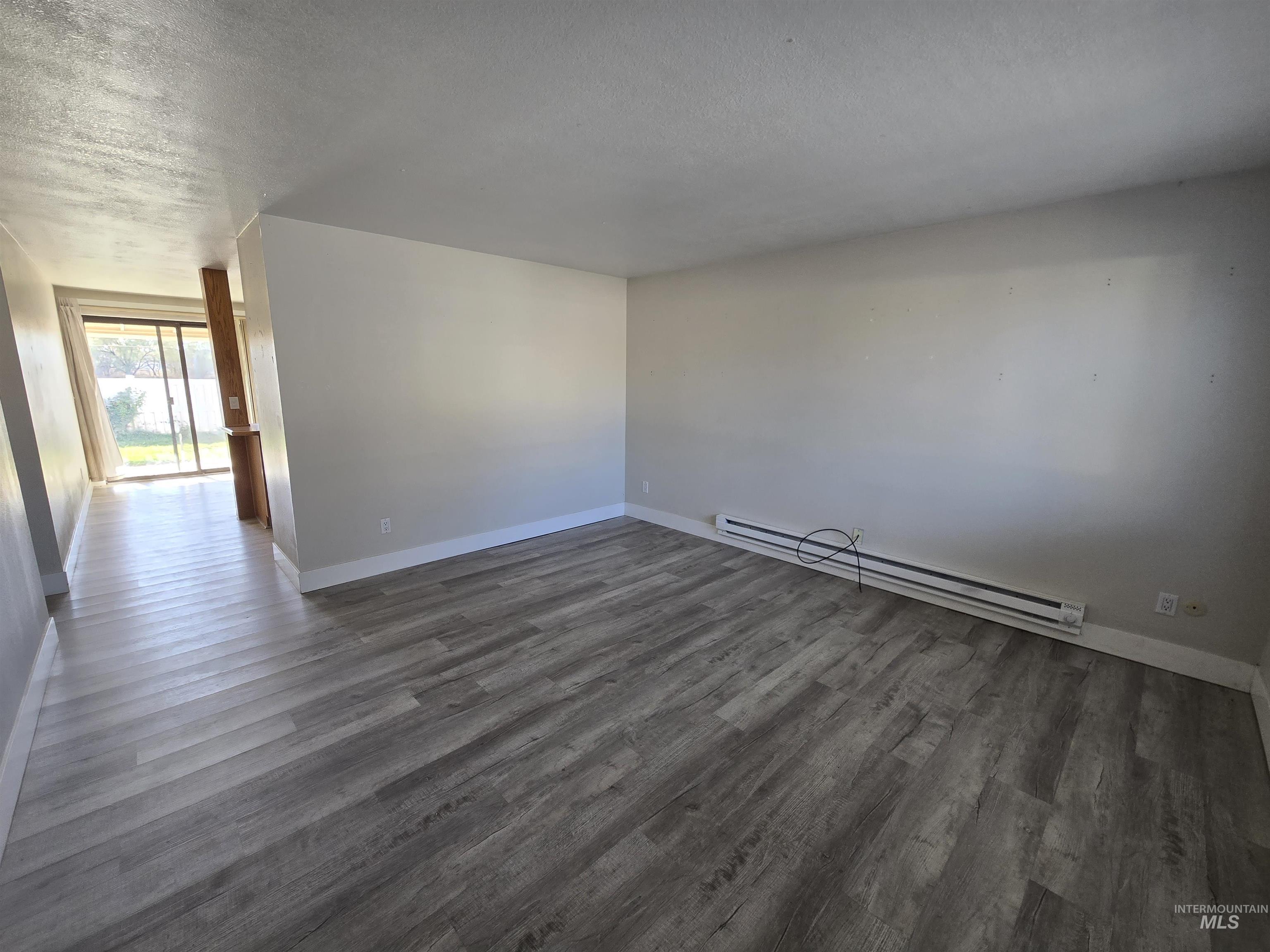 Empty room featuring baseboard heating, a textured ceiling, and dark wood finished floors