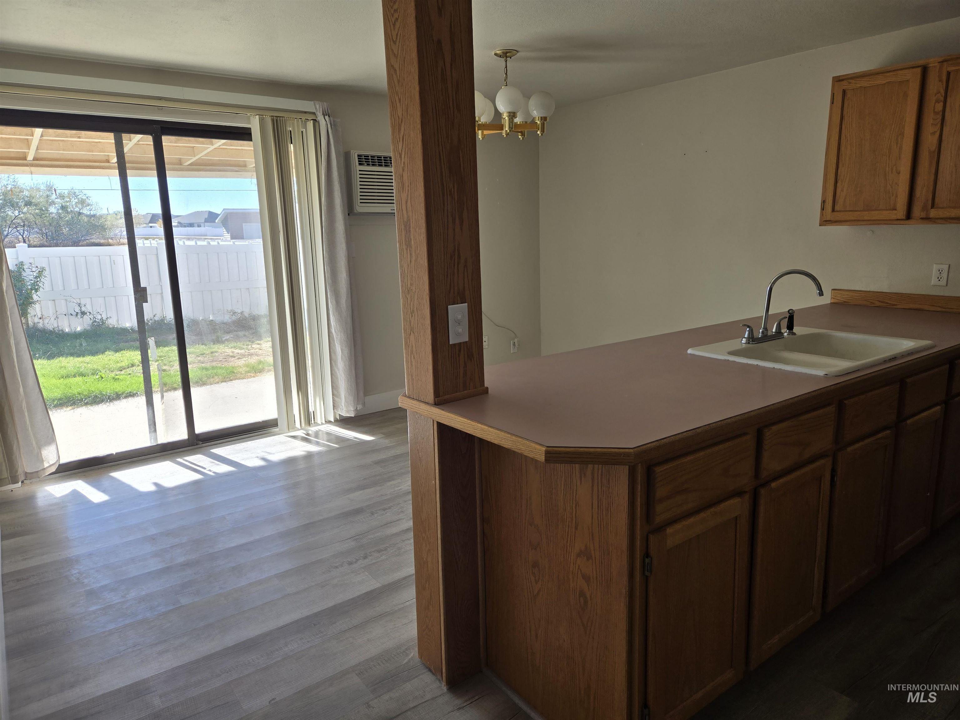 Kitchen featuring dark wood finished floors, brown cabinetry, a peninsula, pendant lighting, and a chandelier