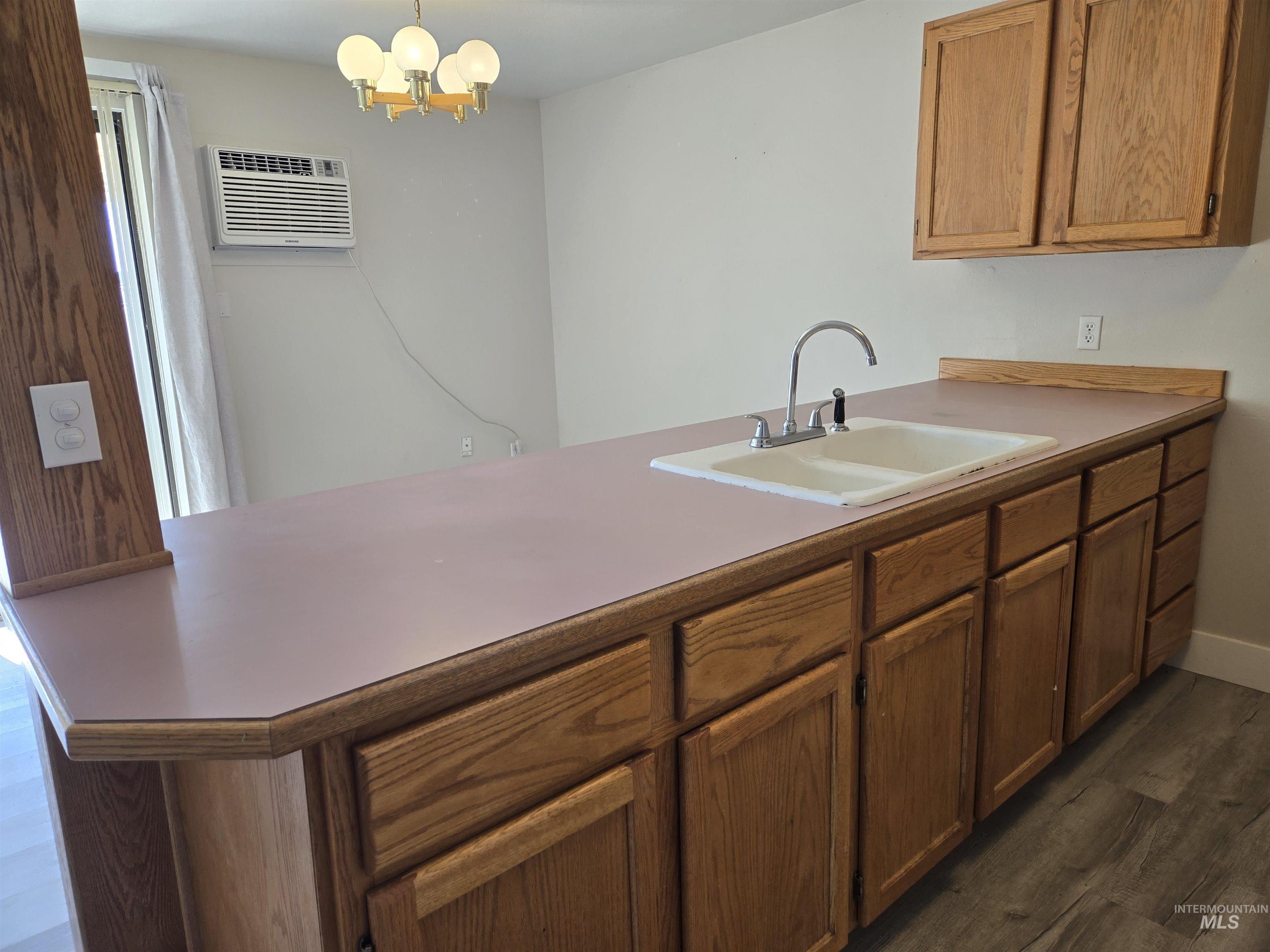 Kitchen with pendant lighting, a peninsula, dark wood-type flooring, light countertops, and a chandelier