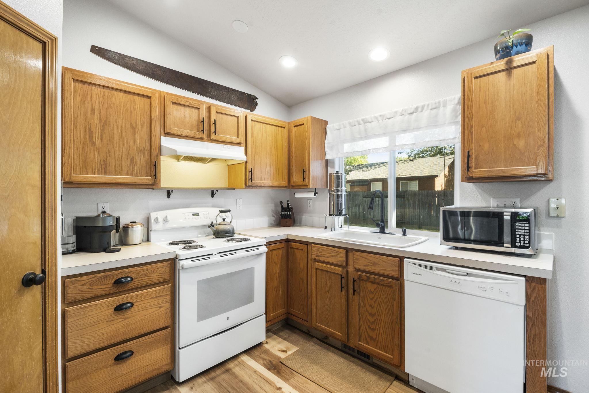 Kitchen with white appliances, light countertops, brown cabinetry, under cabinet range hood, and light wood finished floors