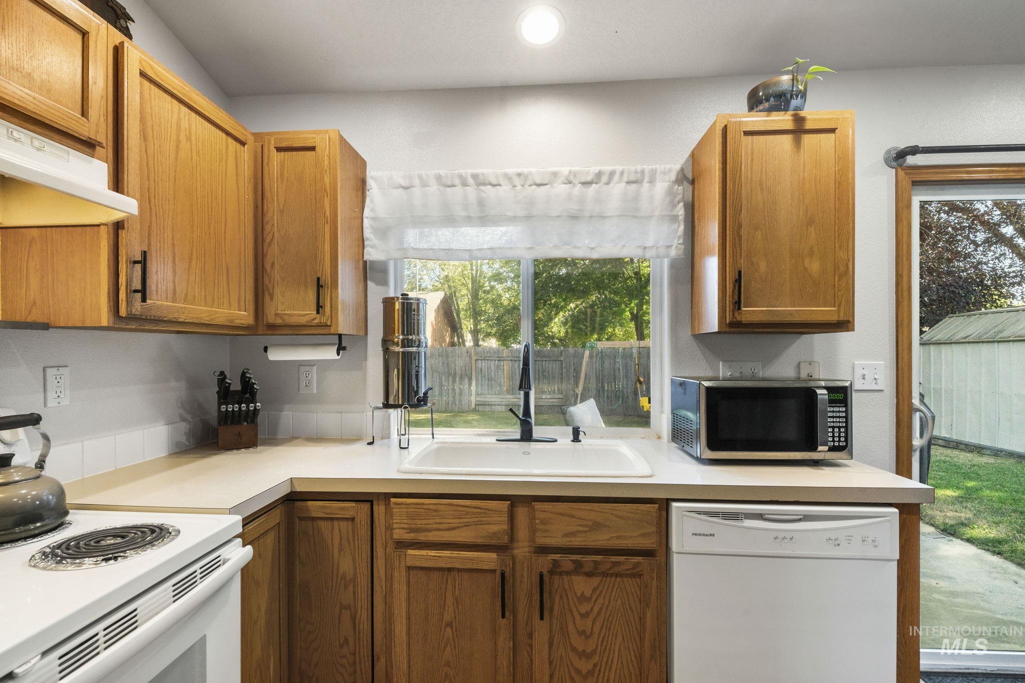 Kitchen featuring white appliances, brown cabinets, light countertops, under cabinet range hood, and recessed lighting