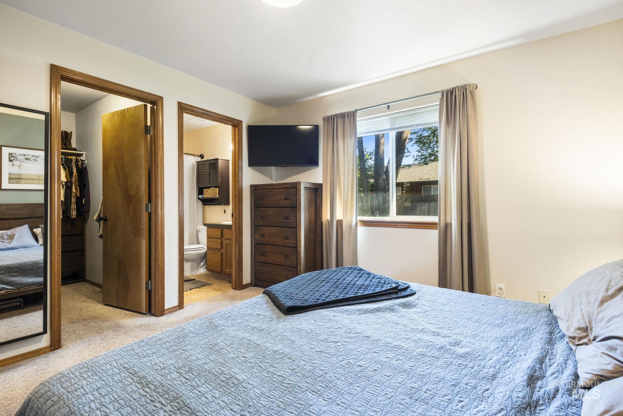 Bedroom featuring light carpet, a spacious closet, and ensuite bath