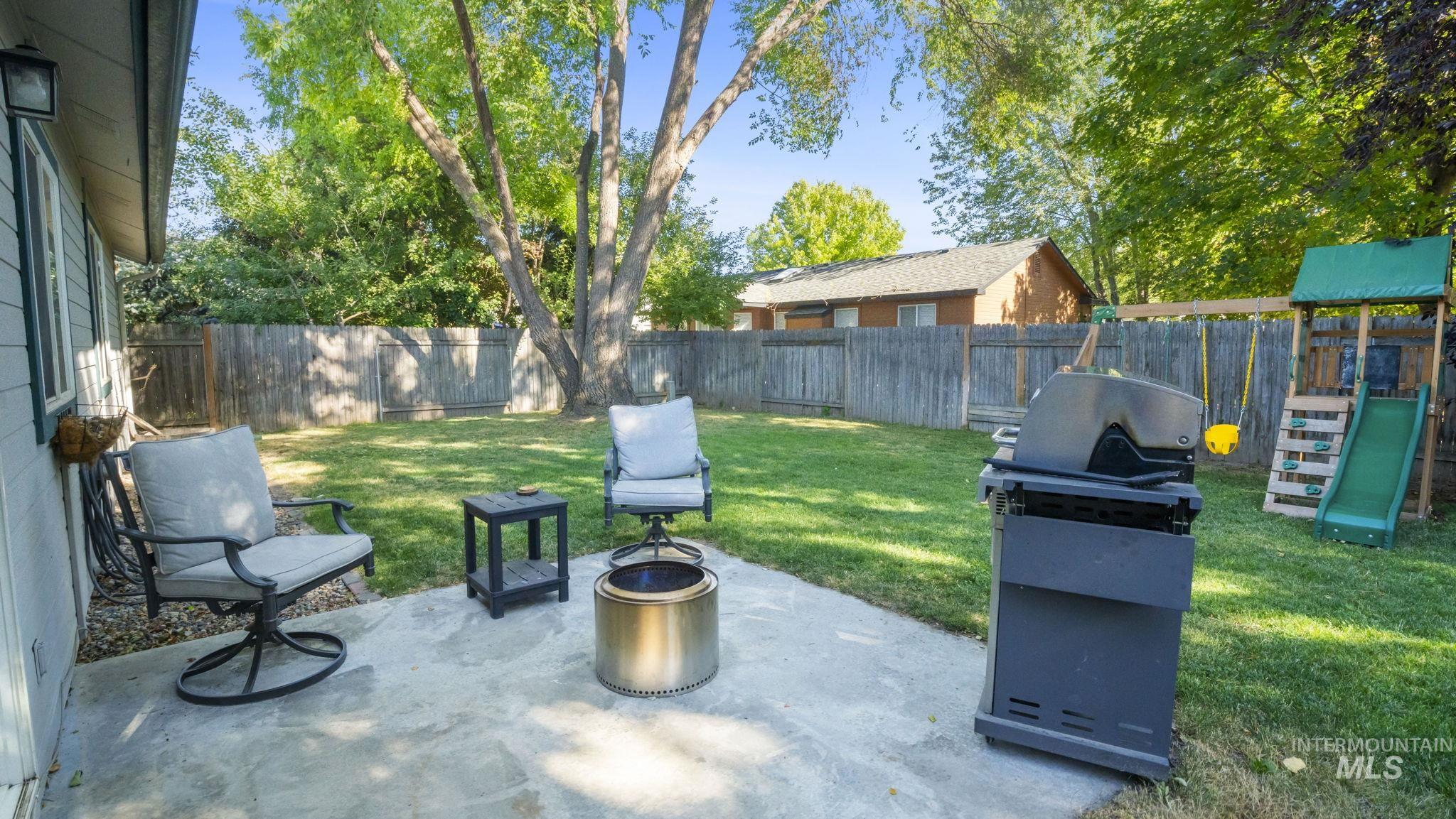 Fenced backyard featuring a patio, a fire pit, area for grilling, and a playground