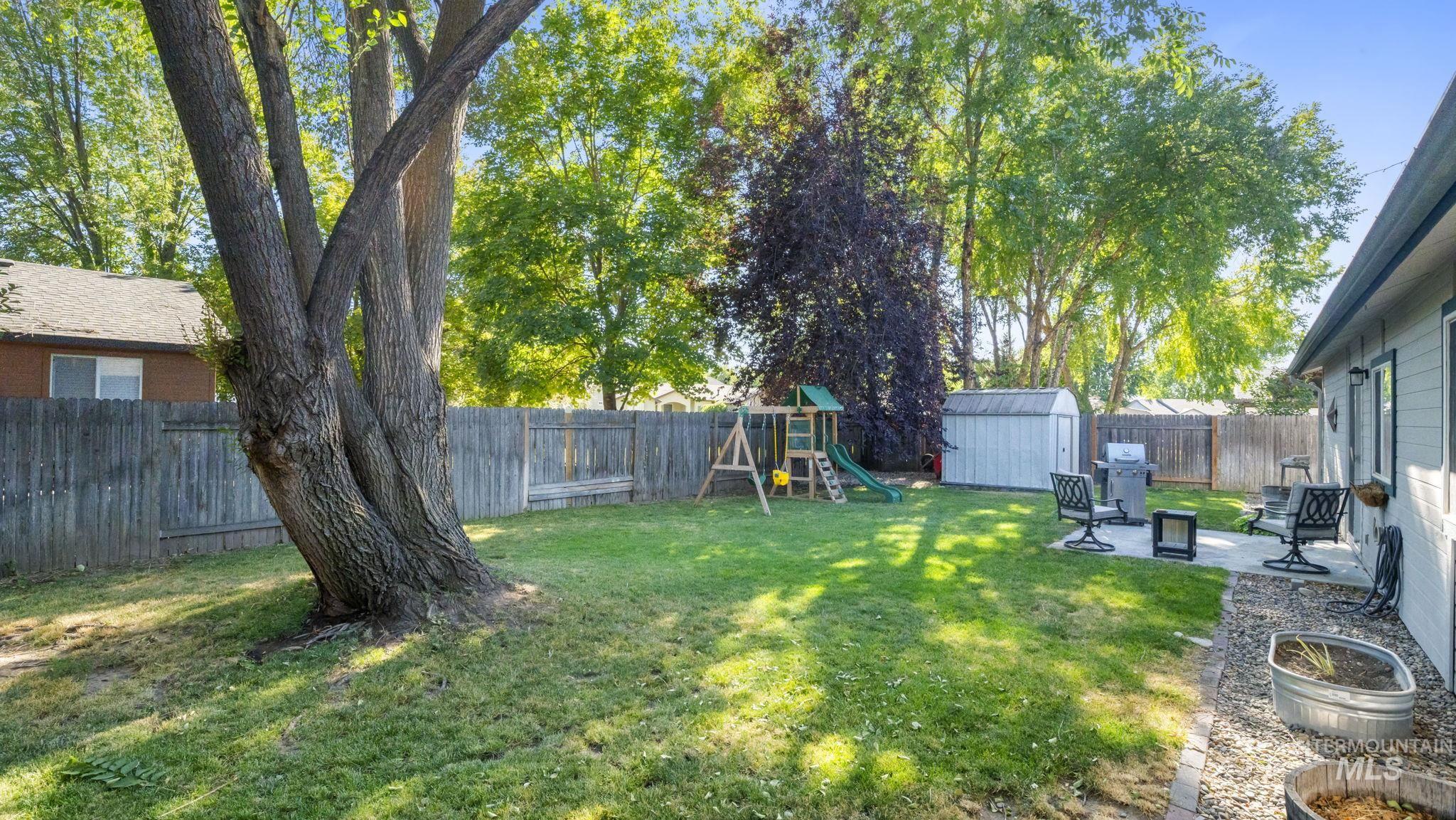 Fenced backyard featuring a playground, a storage unit, and a patio area