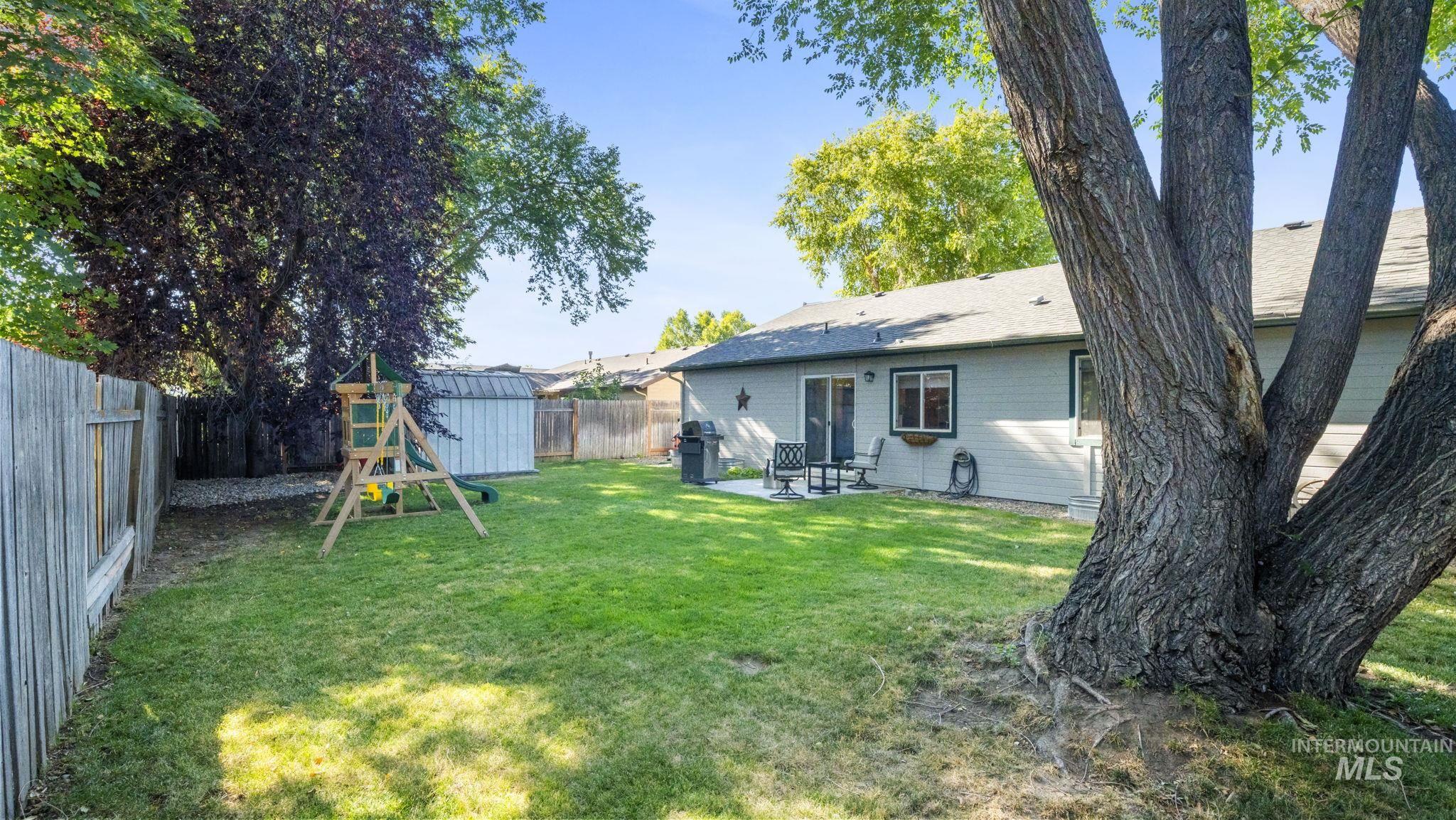 Fenced backyard featuring a patio, a playground, and a storage unit