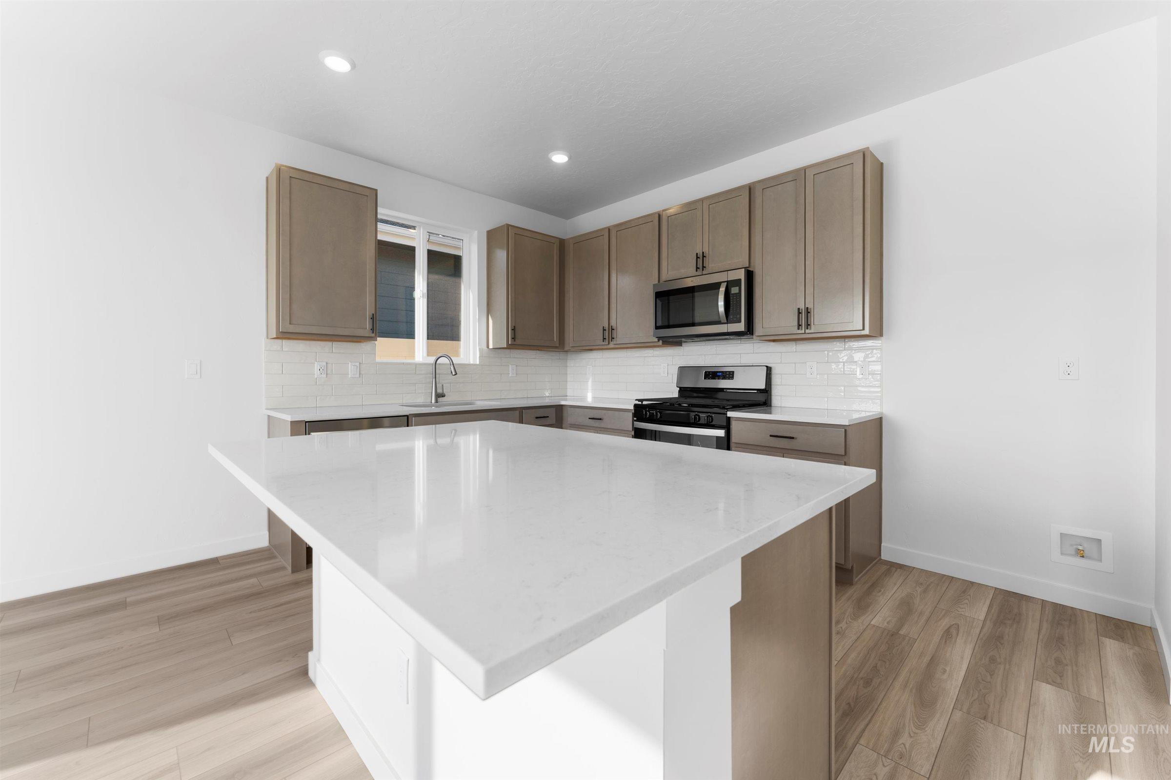 Kitchen featuring stainless steel appliances, light stone countertops, a kitchen island, light wood-style floors, and decorative backsplash