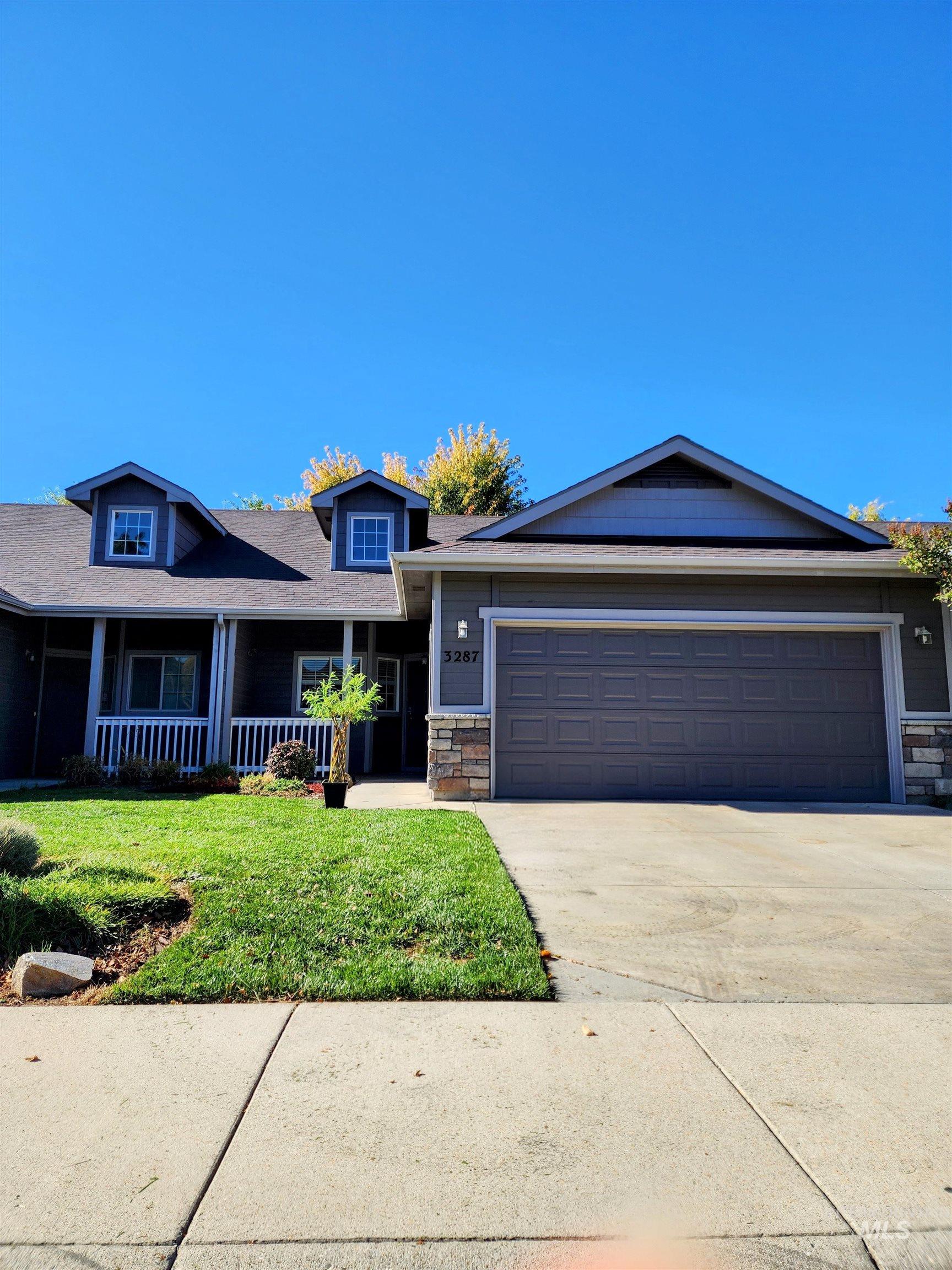 View of front of home featuring stone siding, concrete driveway, a front lawn, a porch, and a garage