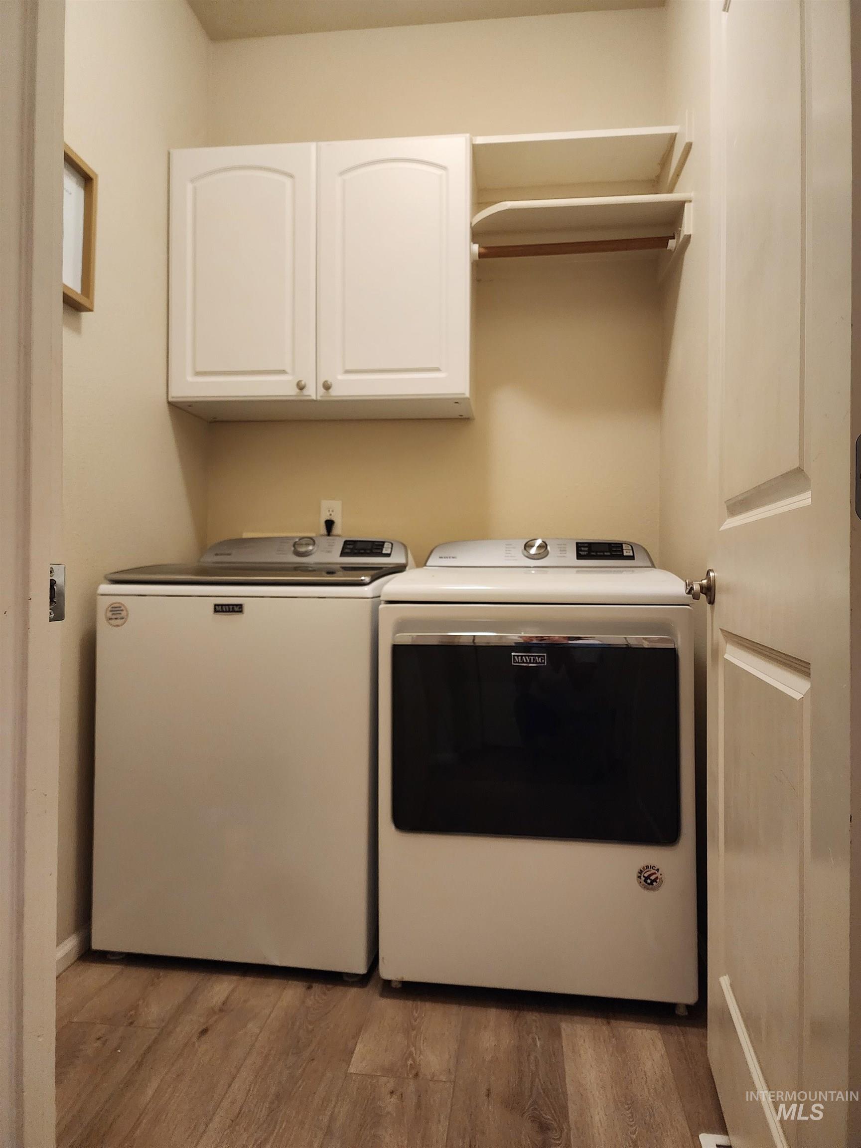 Laundry area with light wood-style flooring, cabinet space, and separate washer and dryer