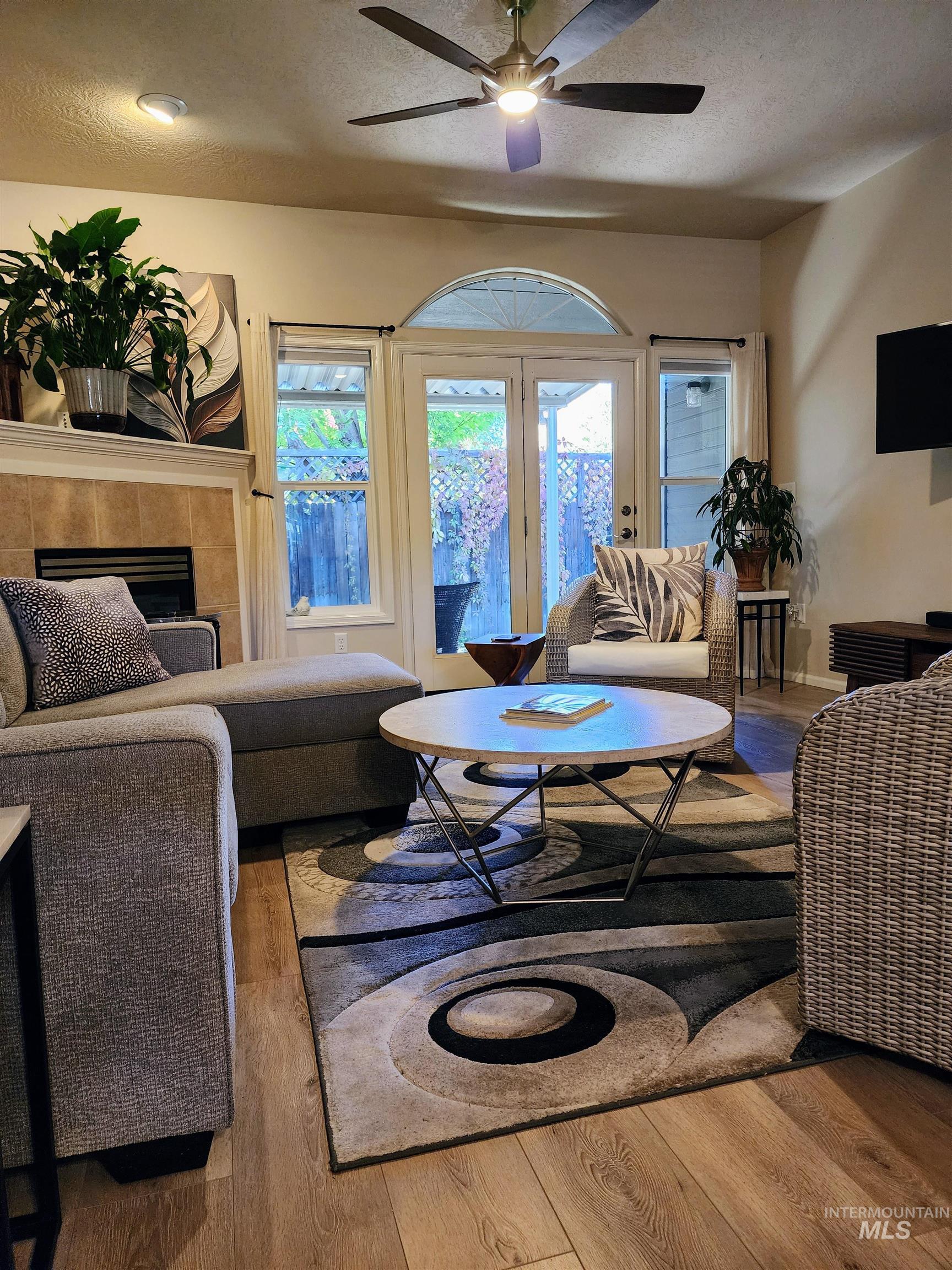 Living area featuring a textured ceiling, wood finished floors, a tiled fireplace, and a ceiling fan