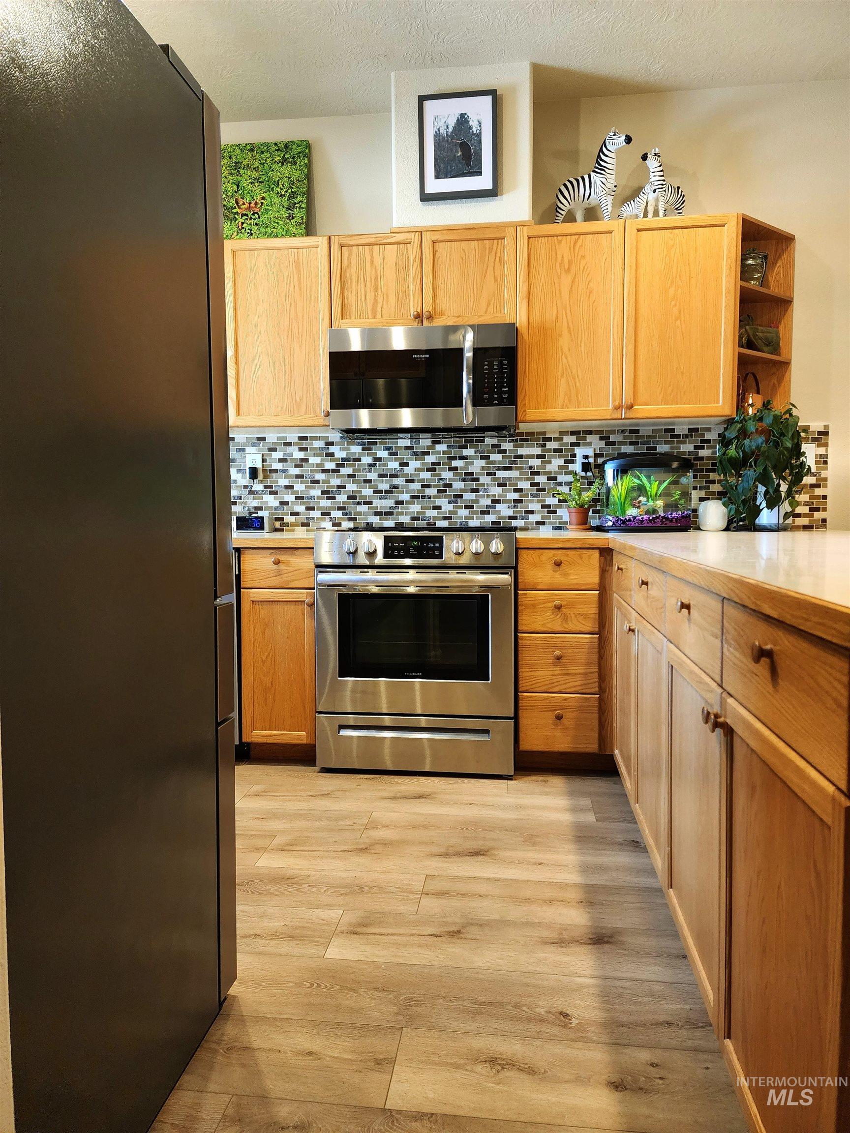 Kitchen featuring stainless steel appliances, light countertops, backsplash, light wood finished floors, and a textured ceiling