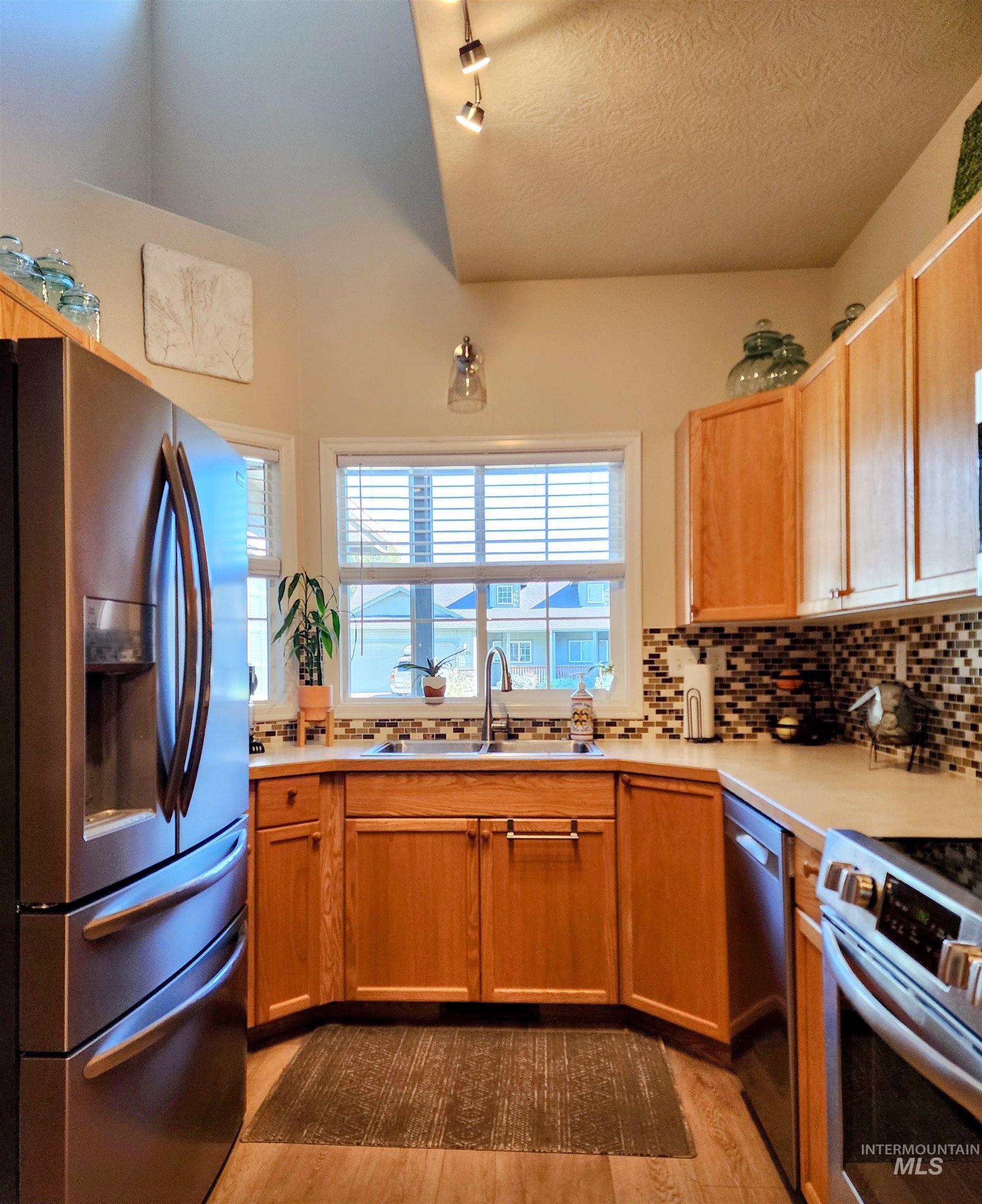 Kitchen featuring stainless steel appliances, light countertops, decorative backsplash, light wood-style flooring, and a textured ceiling