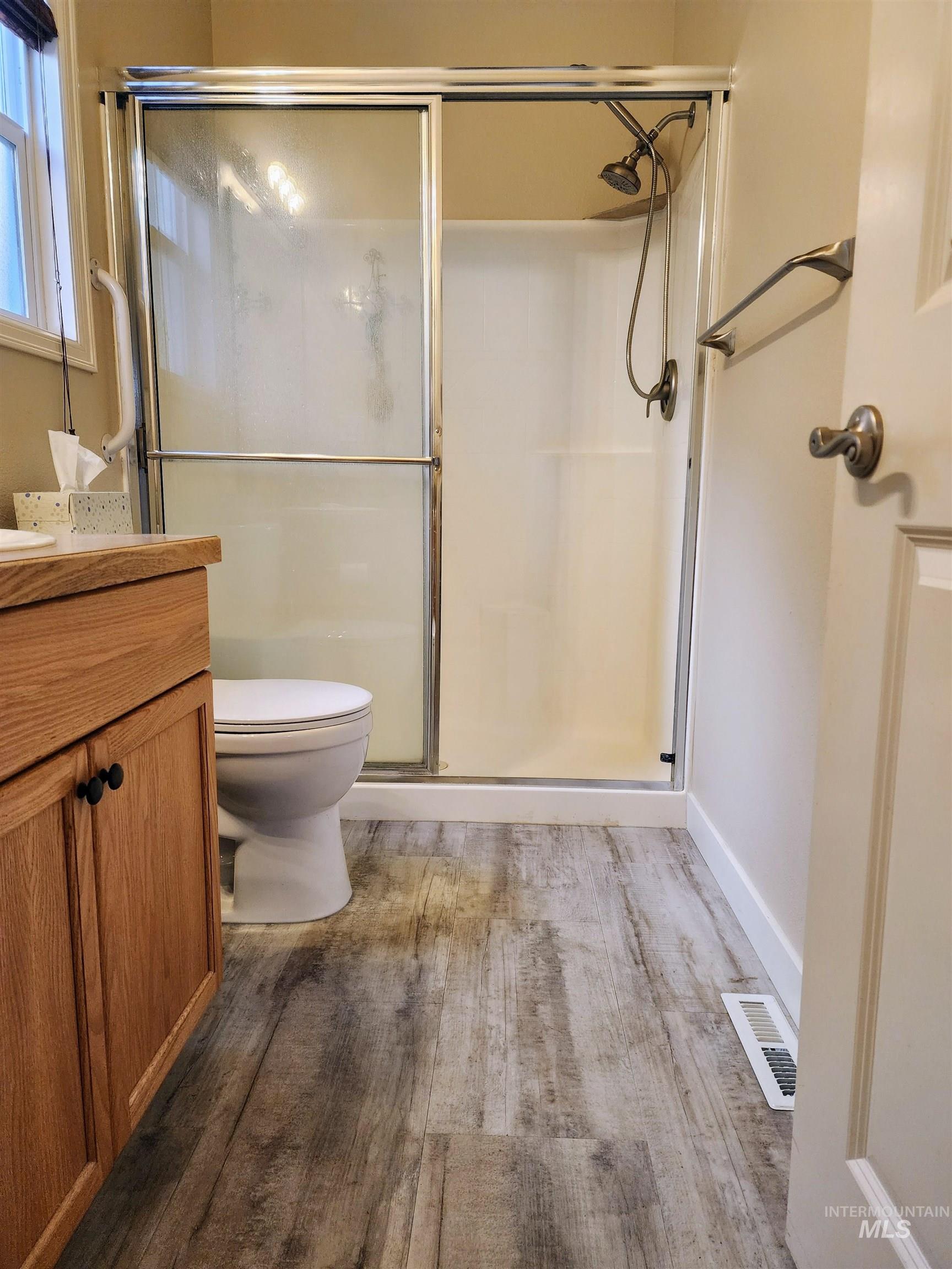 Full bath with light wood finished floors, a stall shower, and vanity