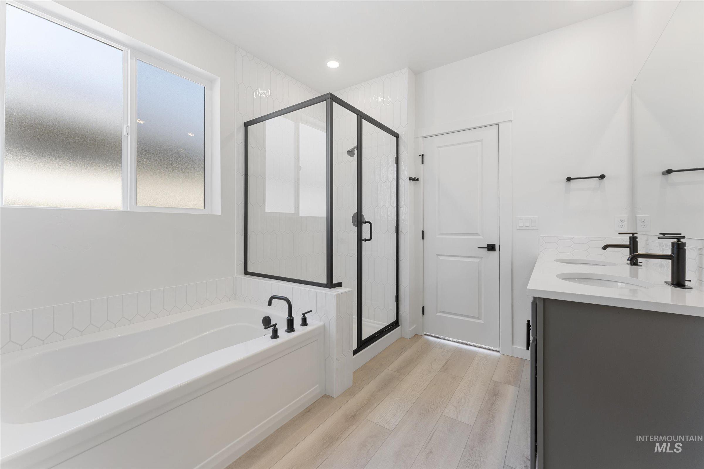 Full bathroom with a bath, double vanity, a shower stall, and light wood-style floors