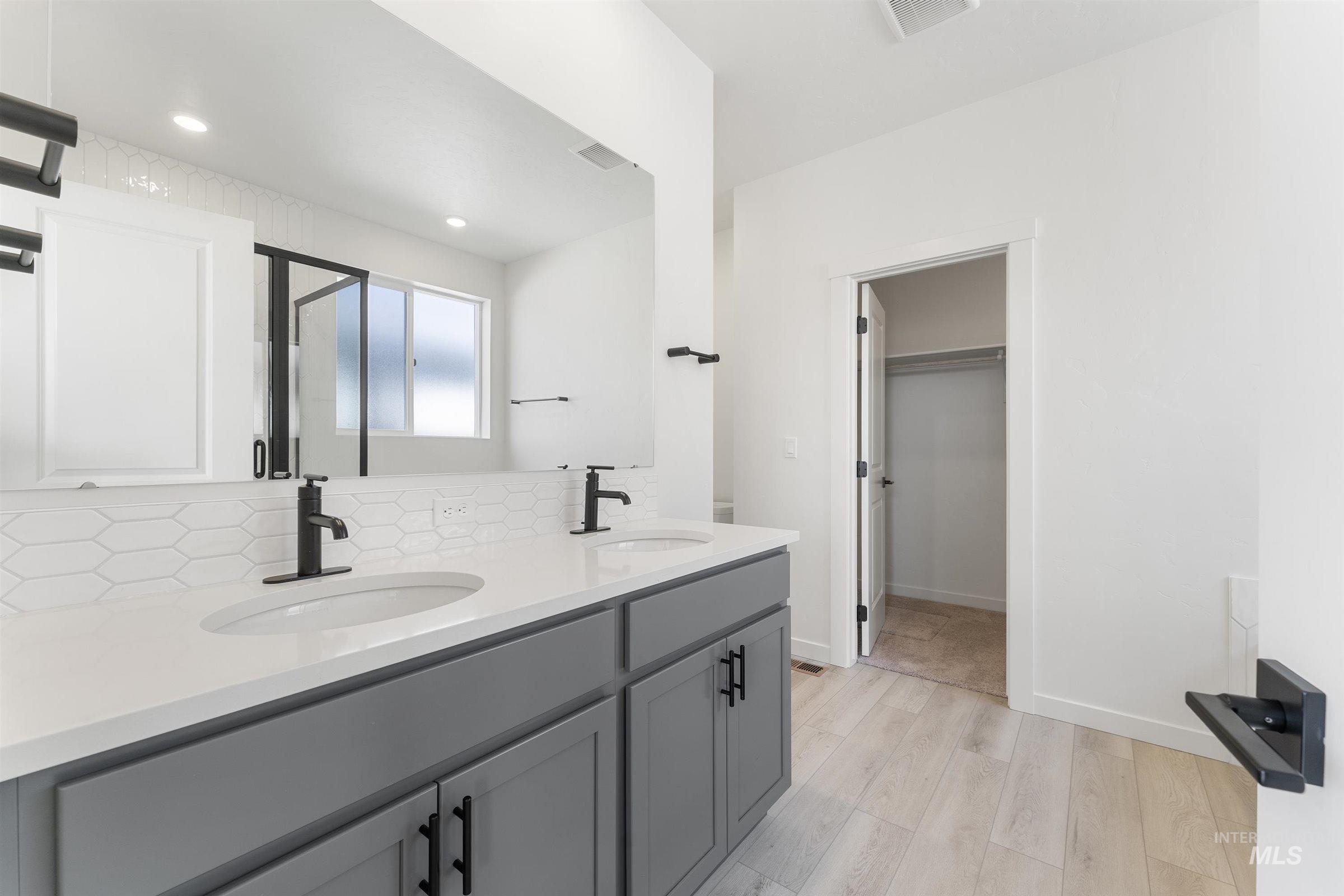 Bathroom featuring double vanity, light wood finished floors, a stall shower, backsplash, and a spacious closet