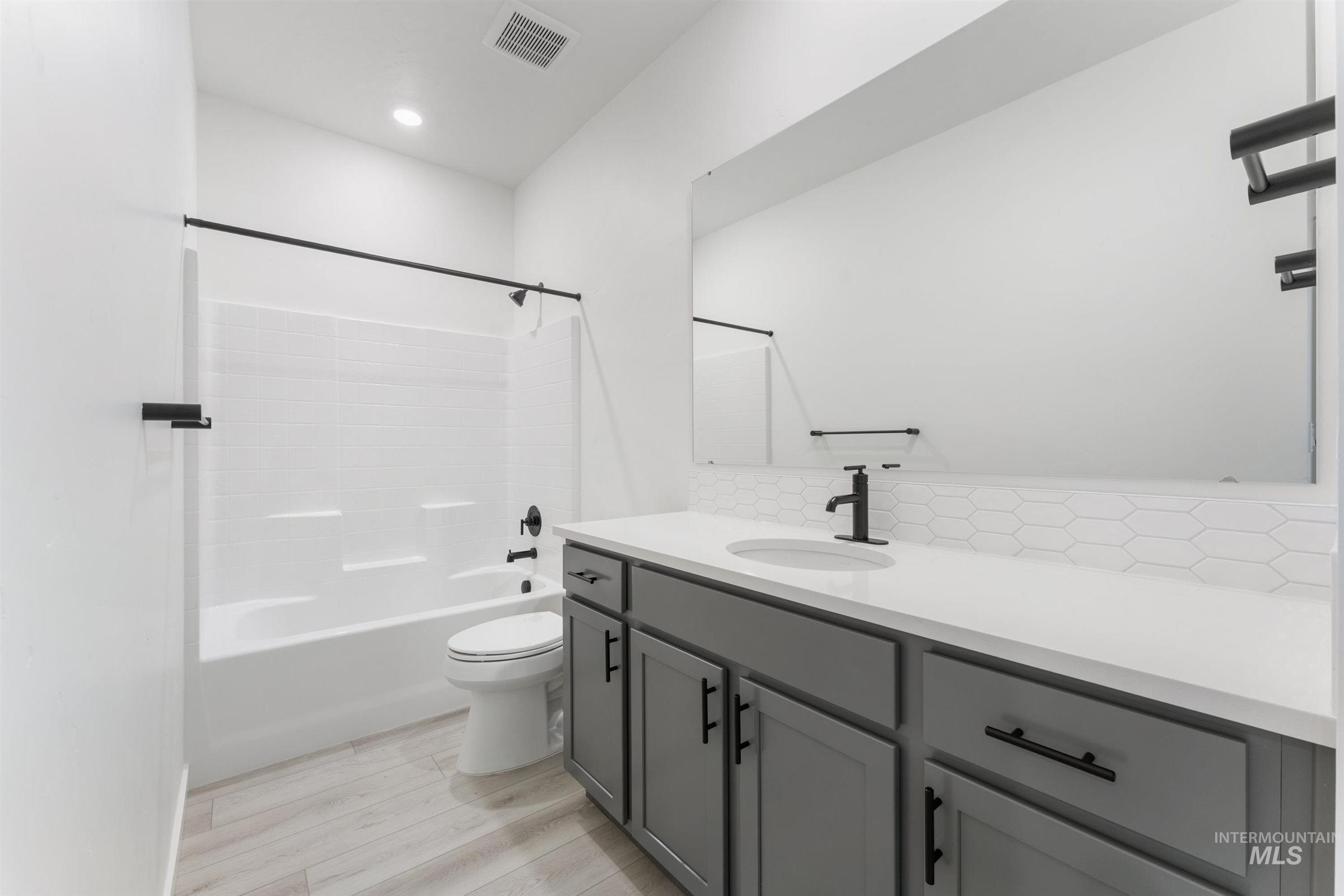 Full bathroom with shower / bathtub combination, vanity, light wood-type flooring, decorative backsplash, and recessed lighting