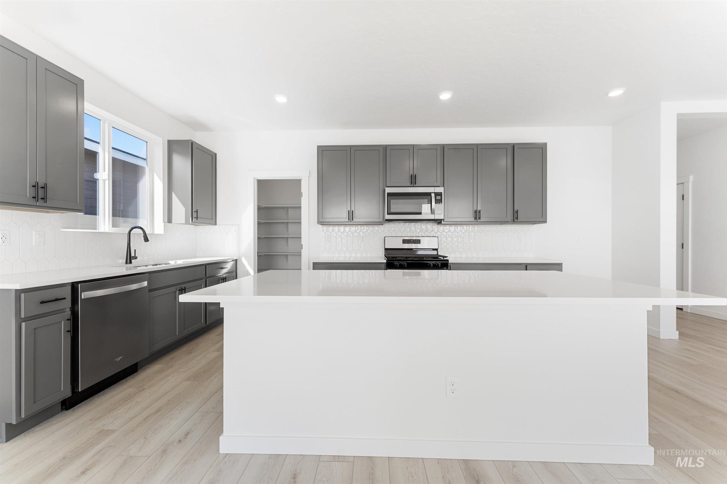 Kitchen with gray cabinets, decorative backsplash, a center island, appliances with stainless steel finishes, and light wood-style flooring