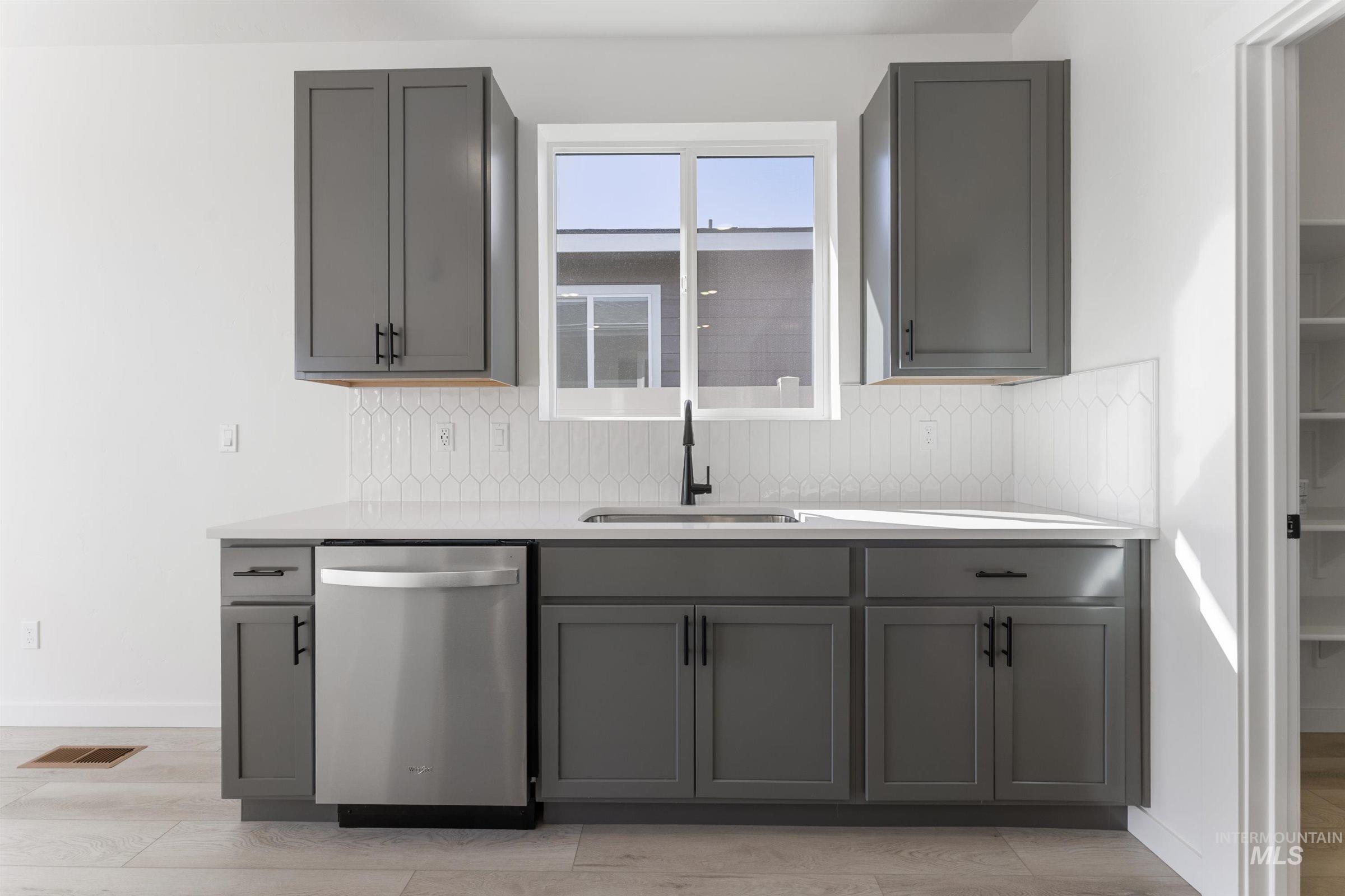 Kitchen with gray cabinets, dishwasher, light wood-style floors, and light stone countertops