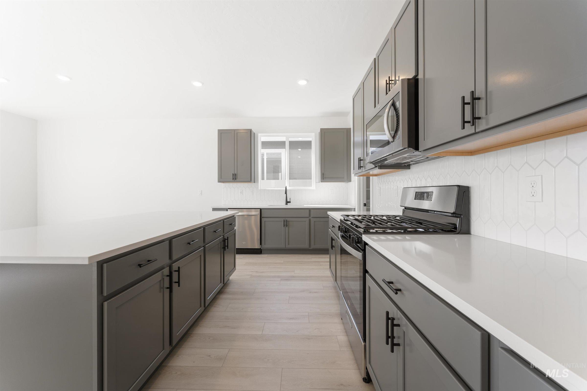Kitchen with stainless steel appliances, decorative backsplash, gray cabinets, recessed lighting, and a kitchen island