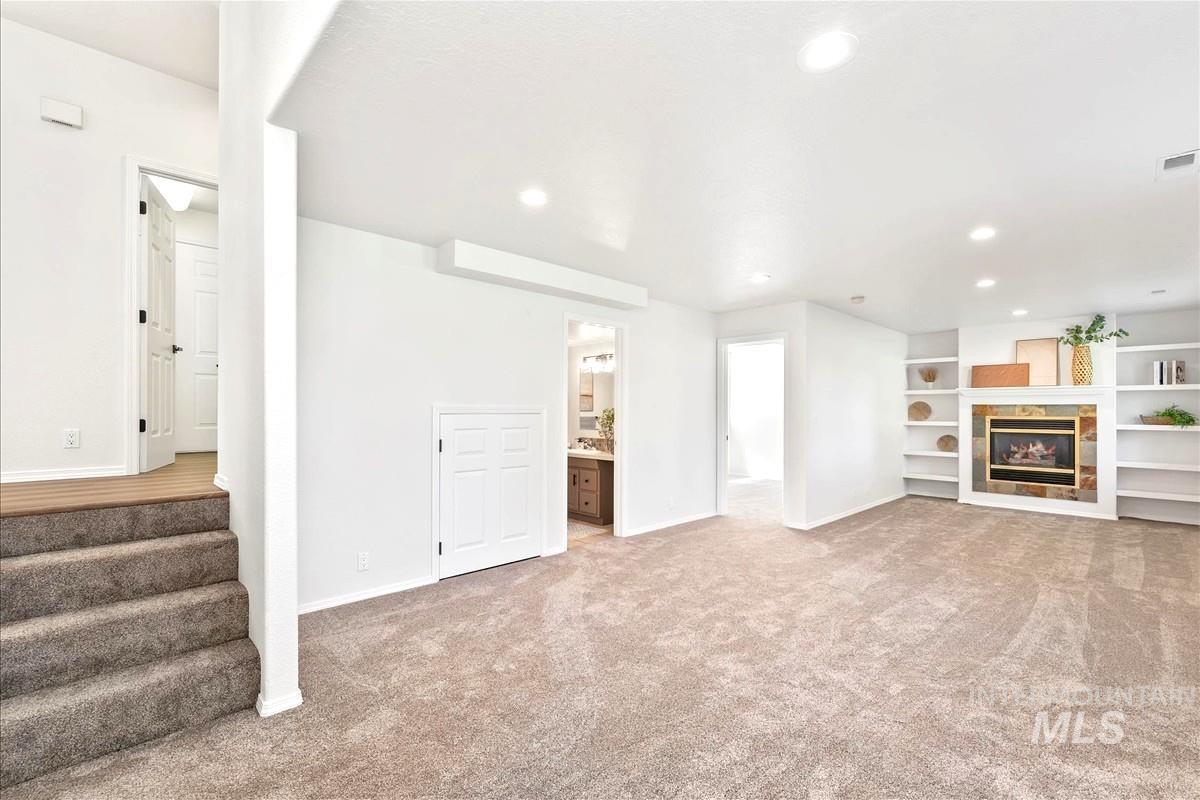 Unfurnished living room with light carpet, recessed lighting, a tile fireplace, and built in shelves
