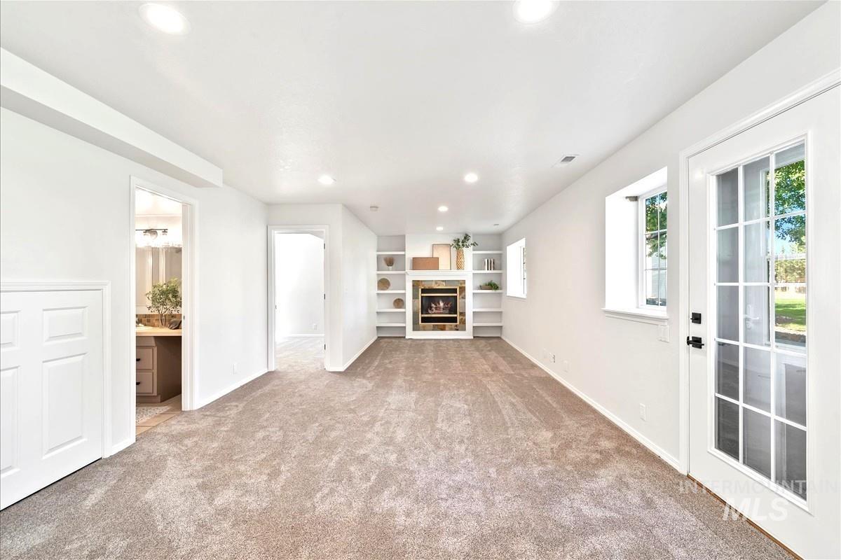 Unfurnished living room featuring recessed lighting, light colored carpet, a glass covered fireplace, and built in shelves