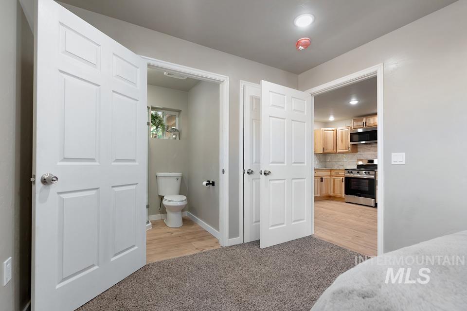 Bedroom with light carpet, ensuite bath, and light wood-type flooring