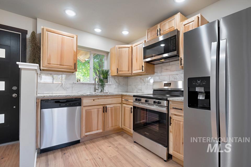 Kitchen featuring stainless steel appliances, light brown cabinetry, backsplash, light wood-style floors, and recessed lighting