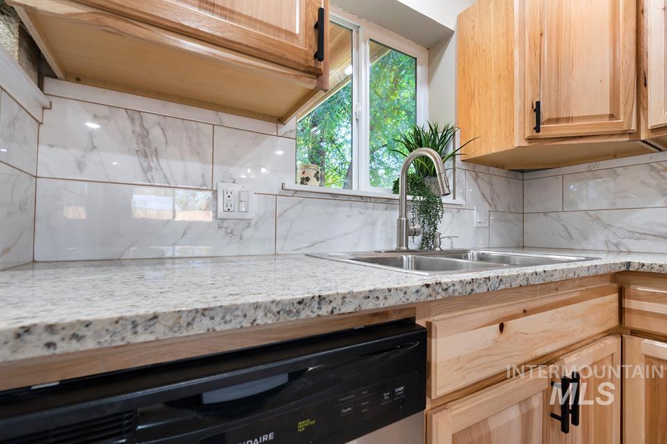 Kitchen featuring light brown cabinets, stainless steel dishwasher, decorative backsplash, and light stone counters