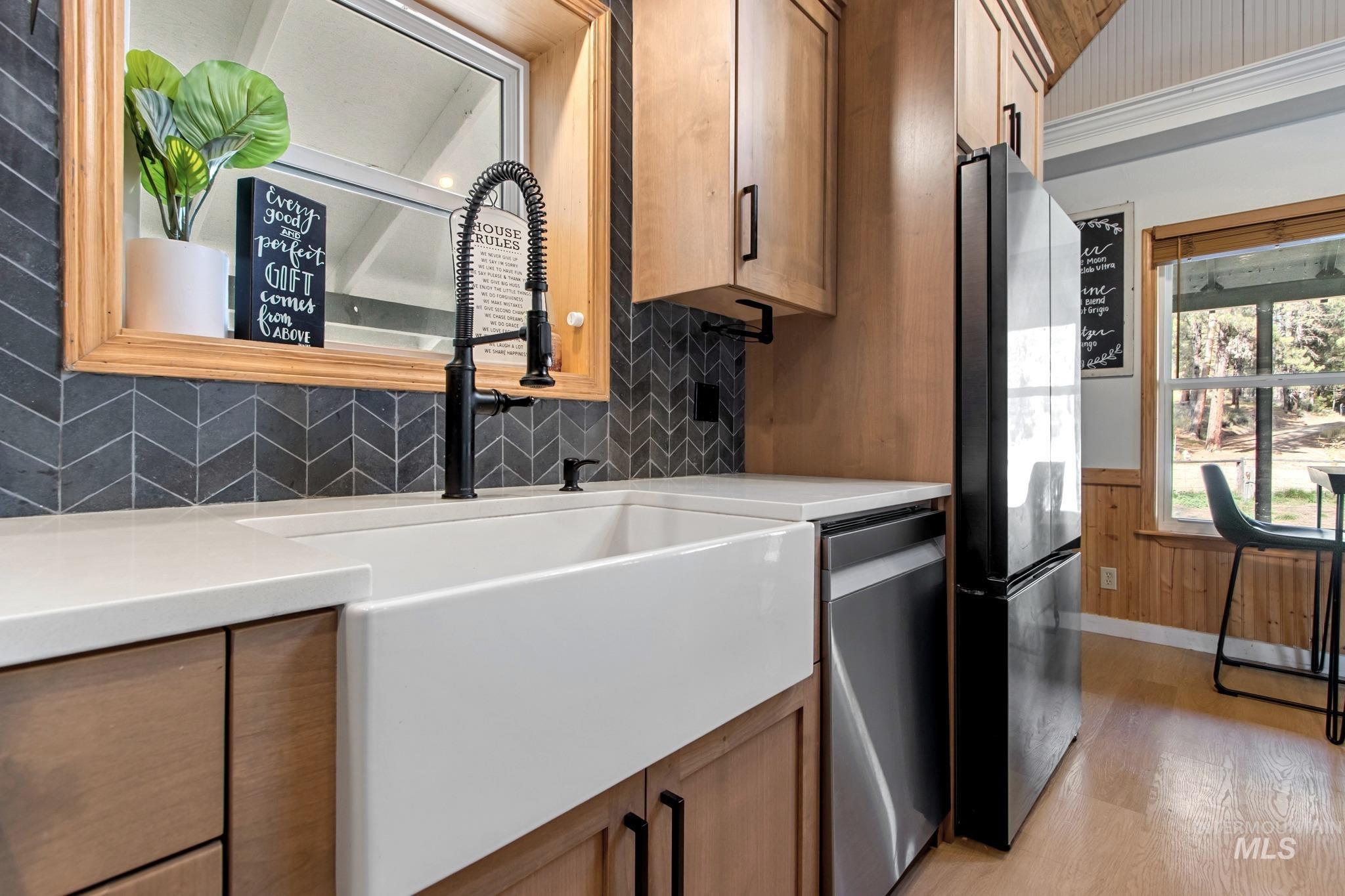 Kitchen with light wood-style floors, freestanding refrigerator, stainless steel dishwasher, wainscoting, and tasteful backsplash