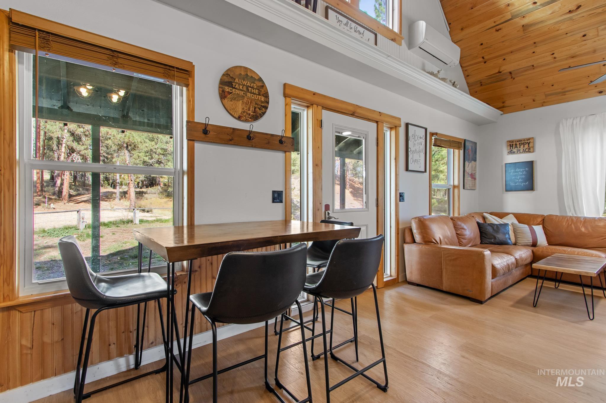 Dining room with wooden ceiling, a wall unit AC, light wood-style flooring, and high vaulted ceiling