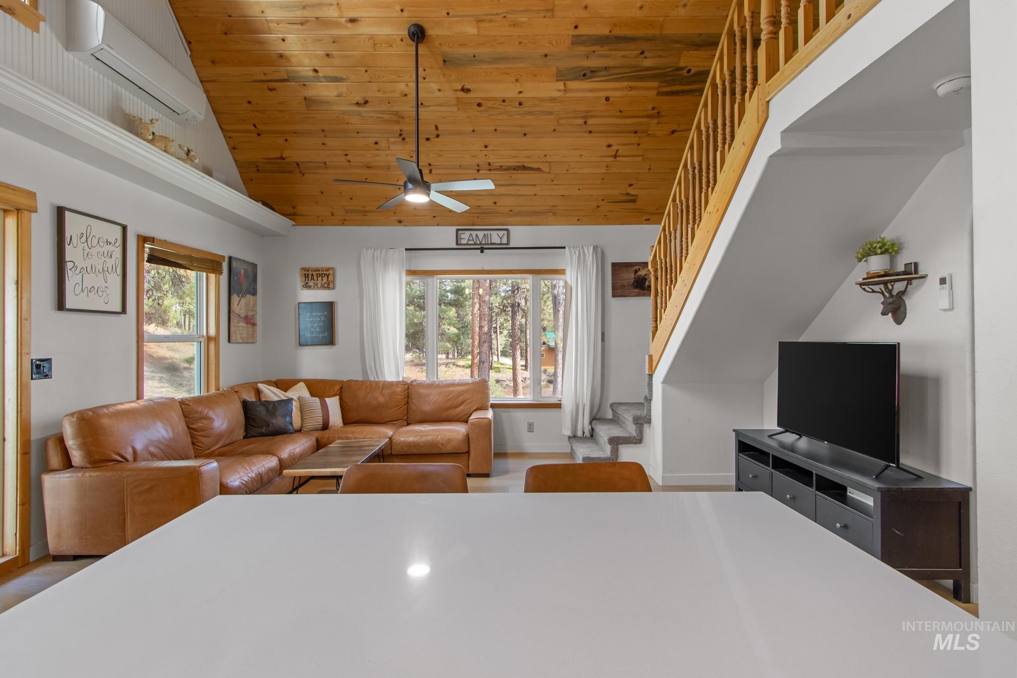 Living area with stairs, a wall mounted air conditioner, wood ceiling, high vaulted ceiling, and light wood finished floors