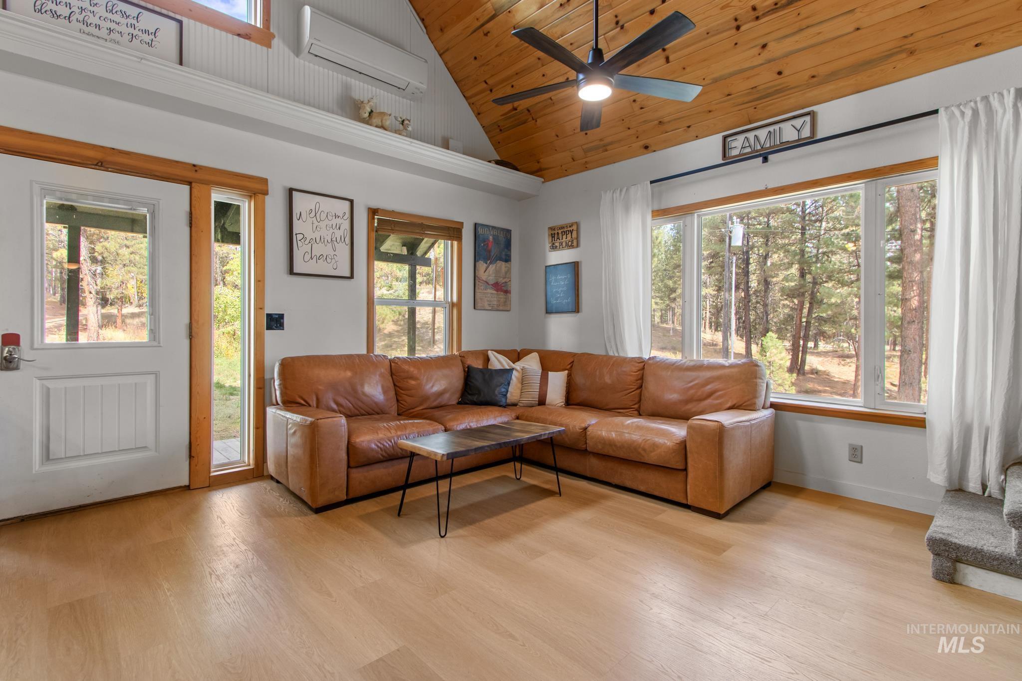 Living room with light wood-style floors, a wall mounted air conditioner, wood ceiling, high vaulted ceiling, and a ceiling fan