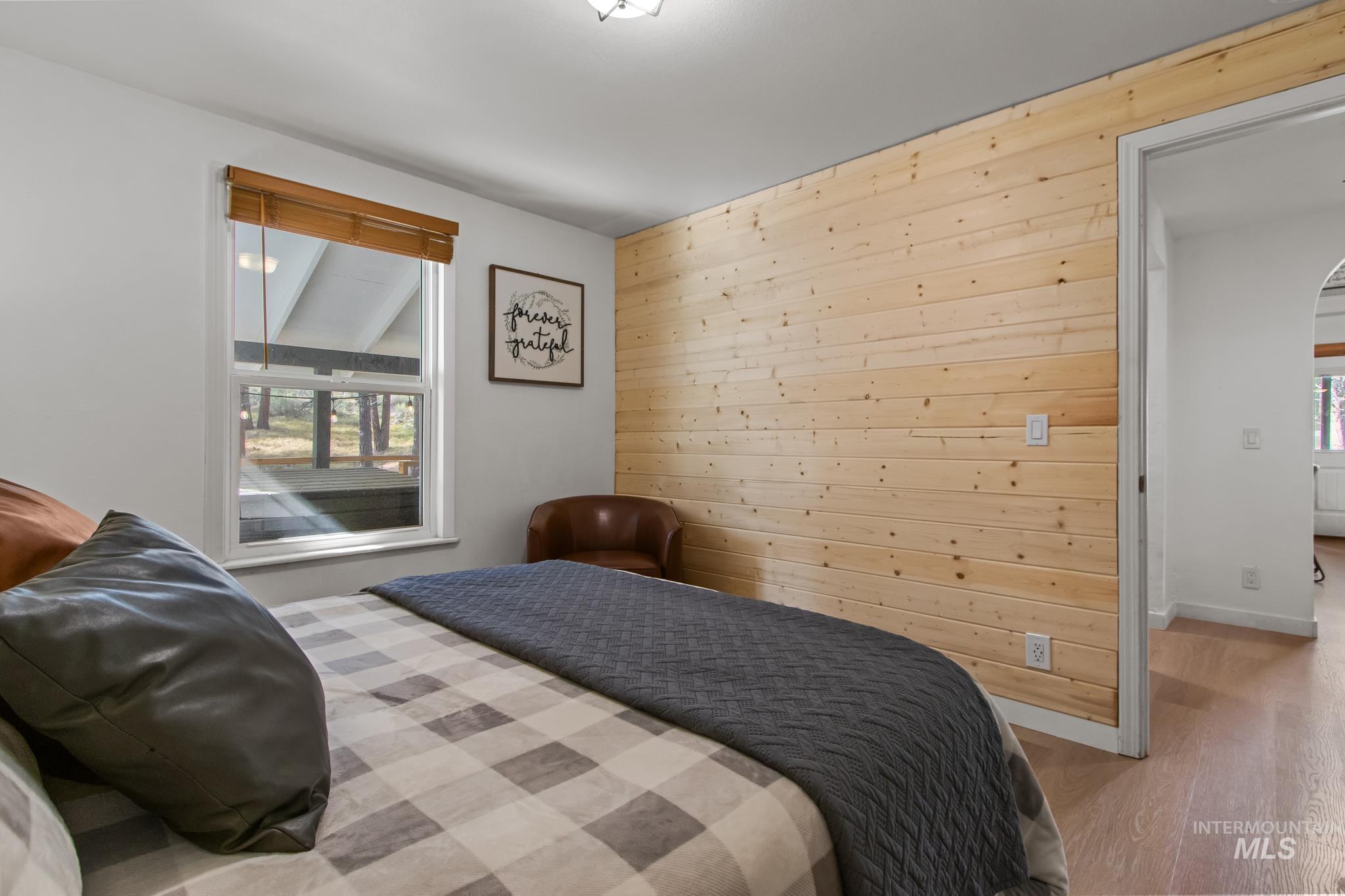Bedroom featuring wooden walls, wood finished floors, multiple windows, and arched walkways