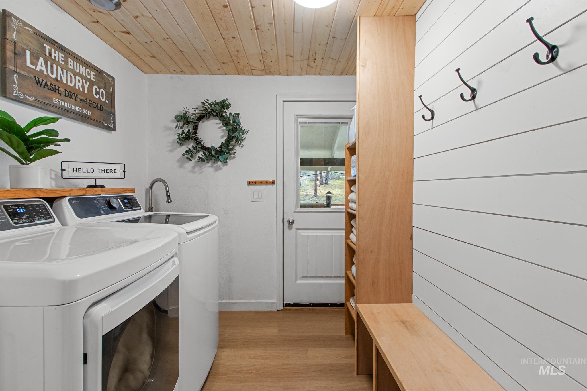 Washroom with light wood finished floors, washing machine and dryer, and wooden ceiling