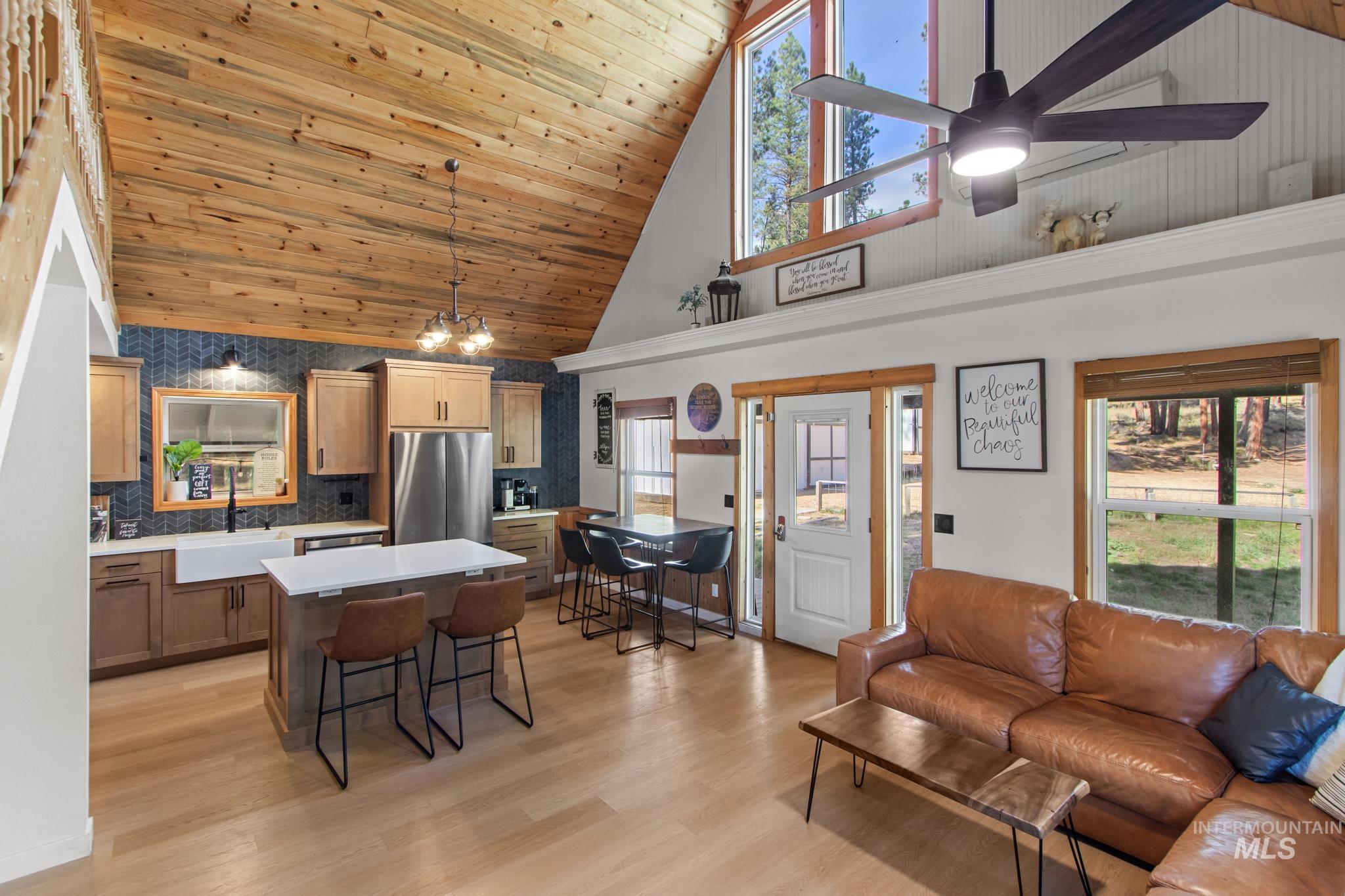 Living area featuring plenty of natural light, high vaulted ceiling, wood ceiling, light wood-type flooring, and a ceiling fan