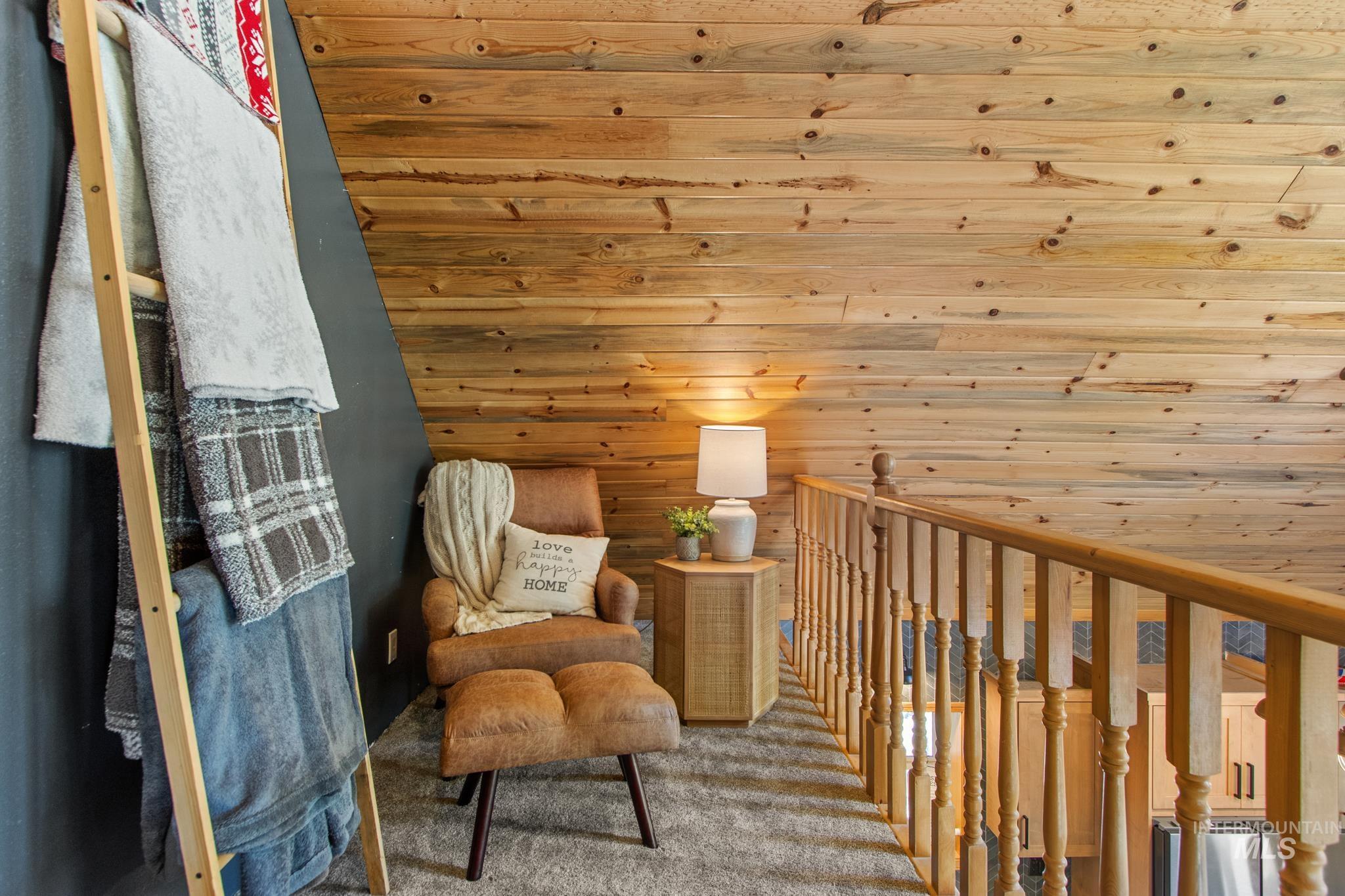 Living area with carpet flooring, wood walls, and an upstairs landing