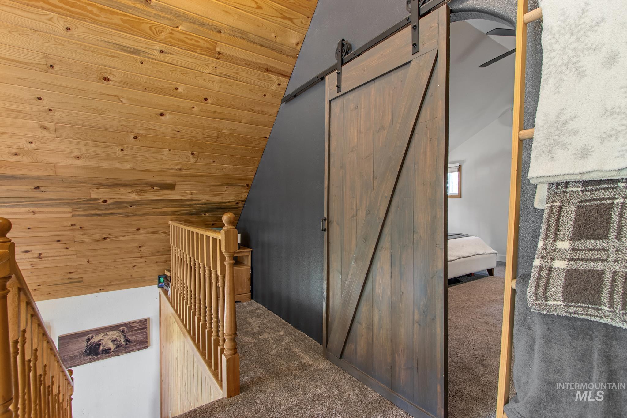Stairway featuring a barn door, carpet flooring, lofted ceiling, wood ceiling, and wooden walls