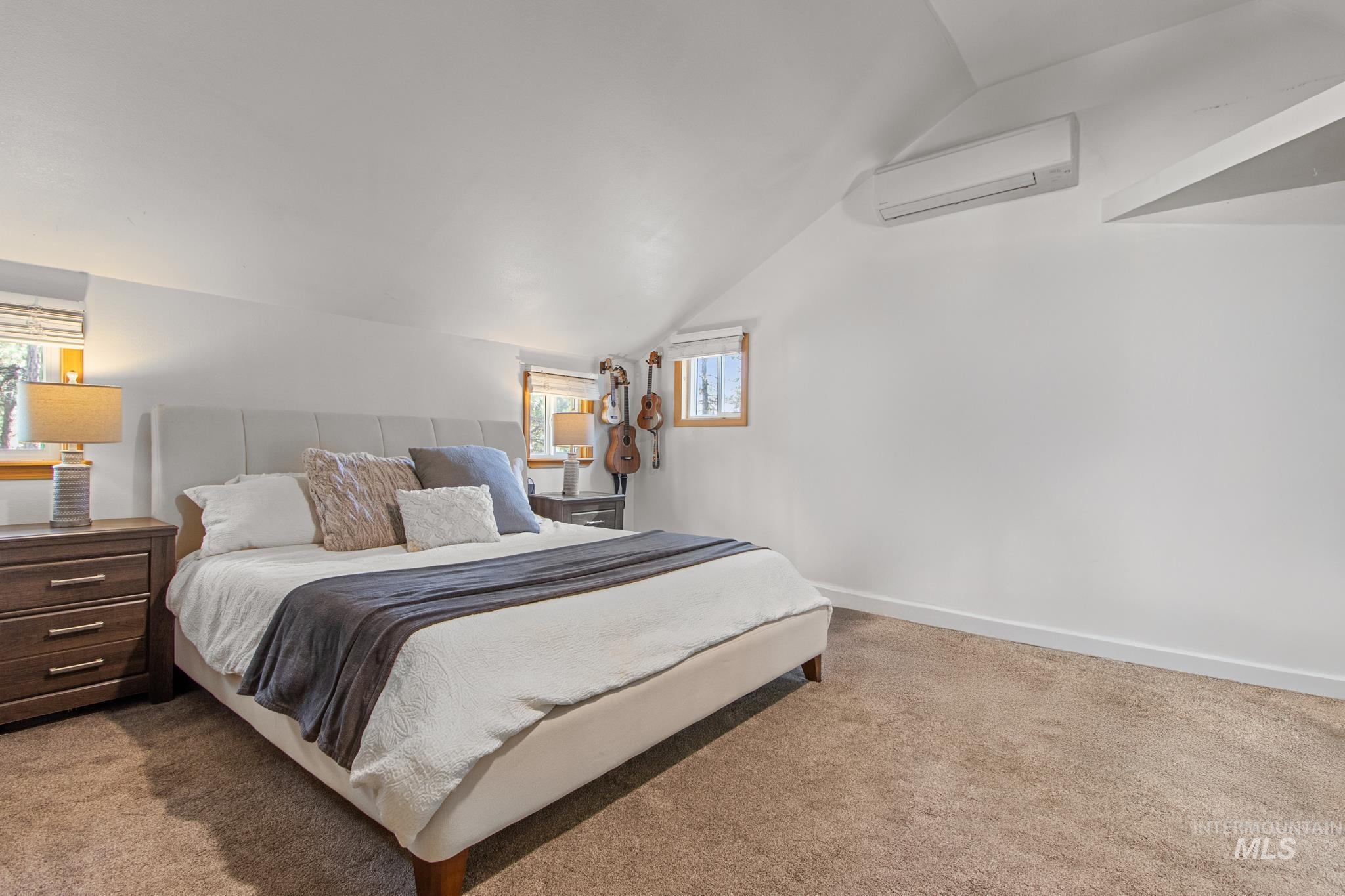 Bedroom with vaulted ceiling, light carpet, and a wall unit AC